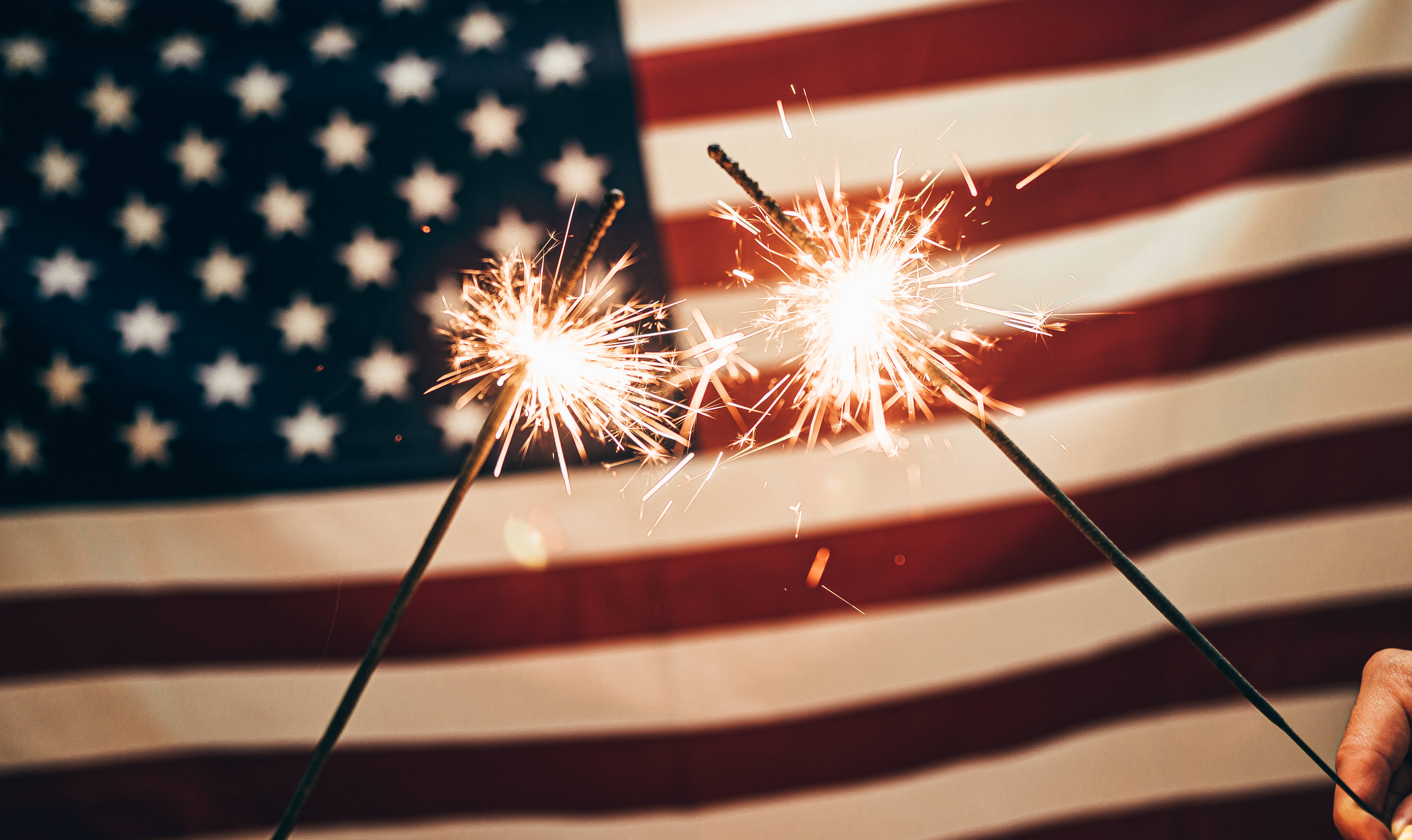 USA flag iPhone 桌布 壁紙 — 兩顆閃爍的煙火在模糊的美國國旗背景下明亮地噼啪作響。
