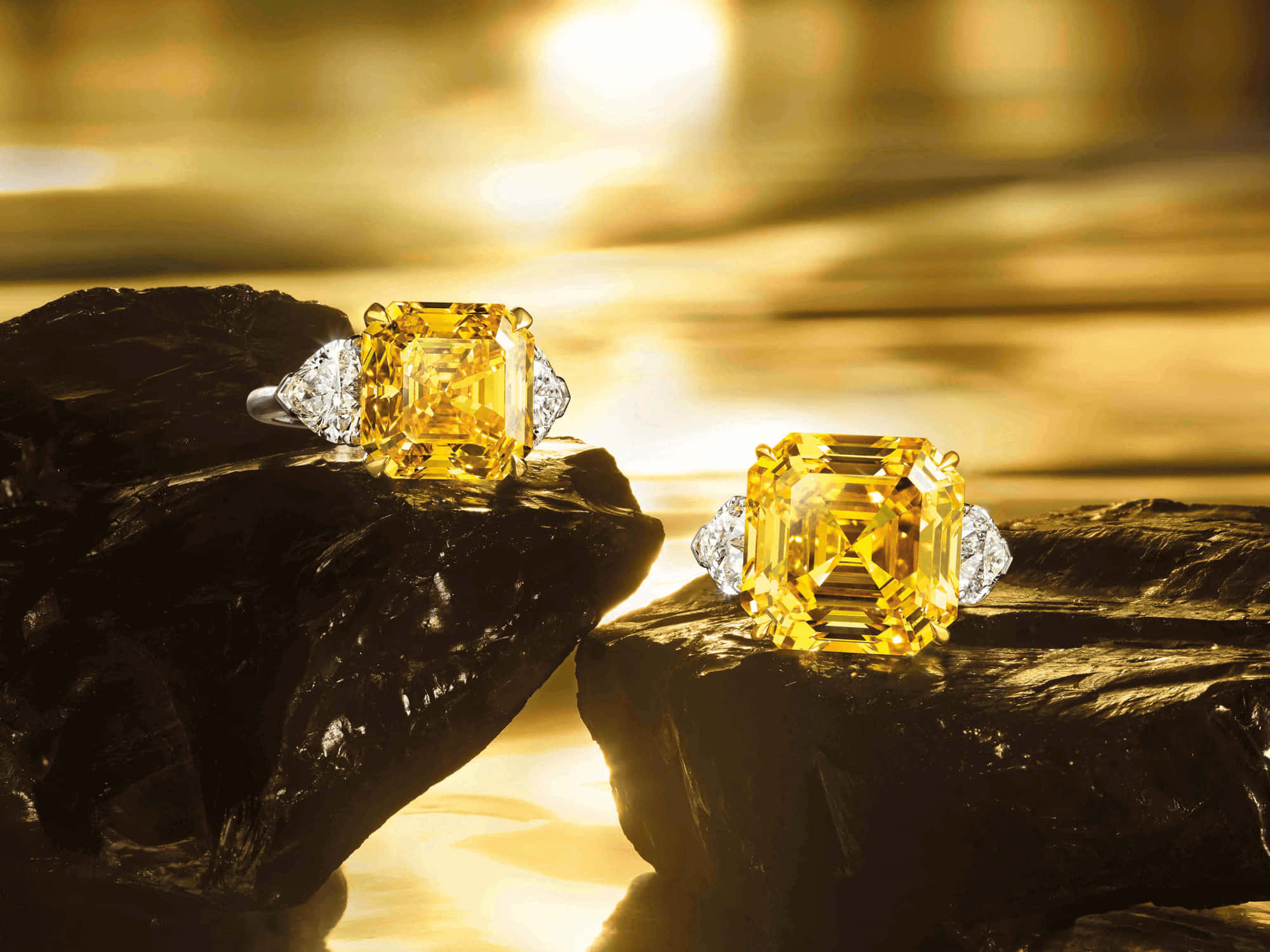 Yellow Diamond 桌布 壁紙 — 兩顆閃耀的黃鑽戒指在深色岩石上閃爍，背景是金色的水面。