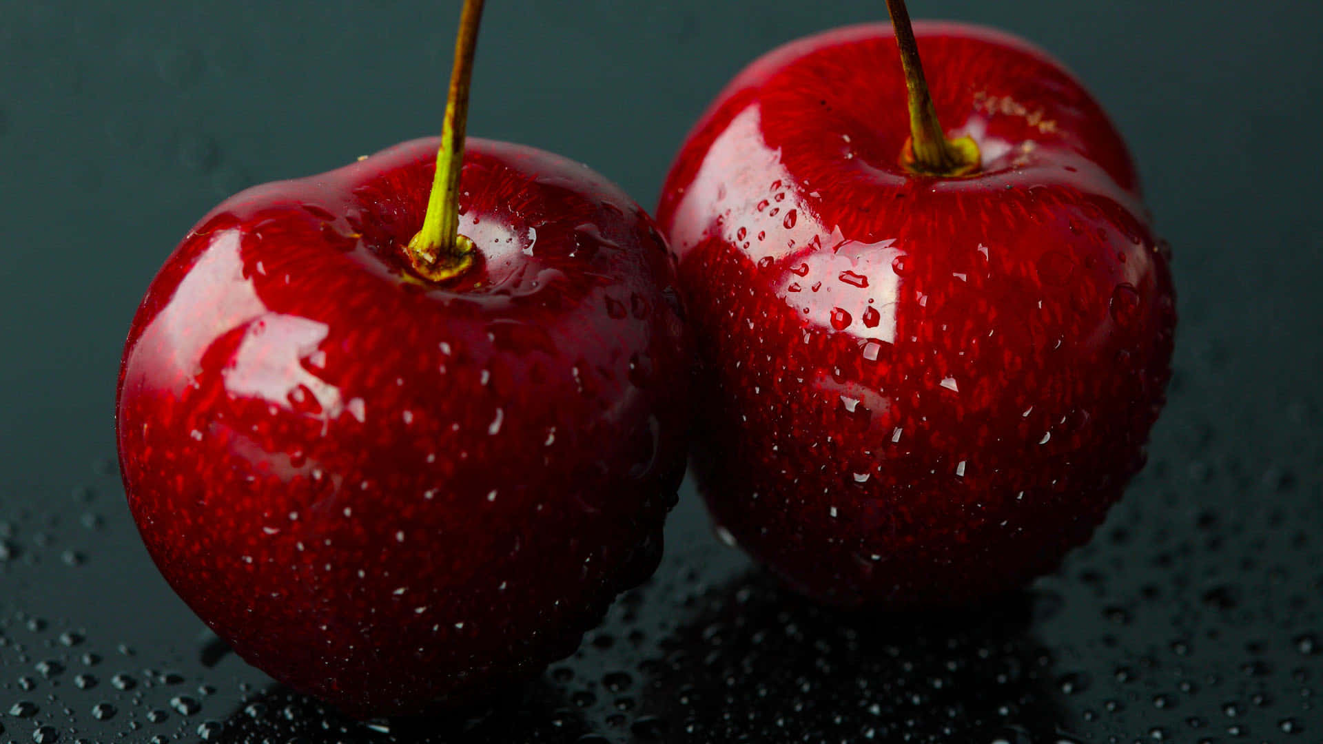 Cherry 桌布 壁紙 — 兩顆閃閃發光的紅櫻桃帶有水珠，放在一個深色潮濕的表面上，反射出它們鮮豔的色彩。