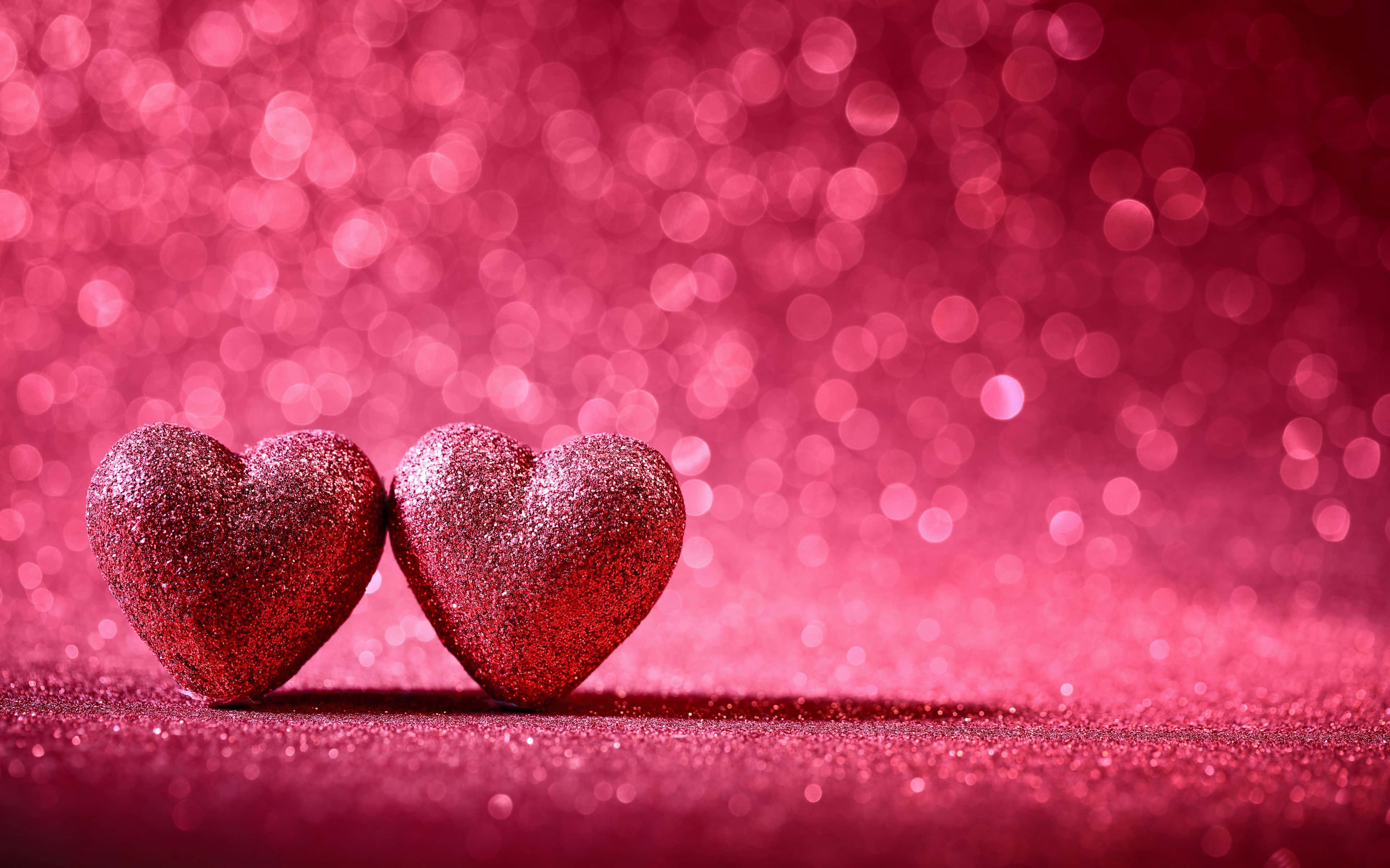 Glitter Pink Hearts 桌布 壁紙 — 兩顆閃閃發光的紅色心形並排放在閃爍的粉紅色表面上，背景為散景效果。