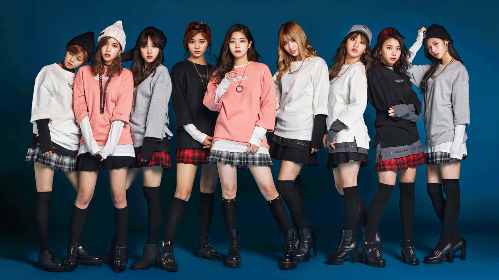 twice 桌布 壁紙 — 八位時尚年輕女性穿著搭配的毛衣、格子裙和黑色靴子，在純藍色攝影棚背景前自信地擺姿勢。