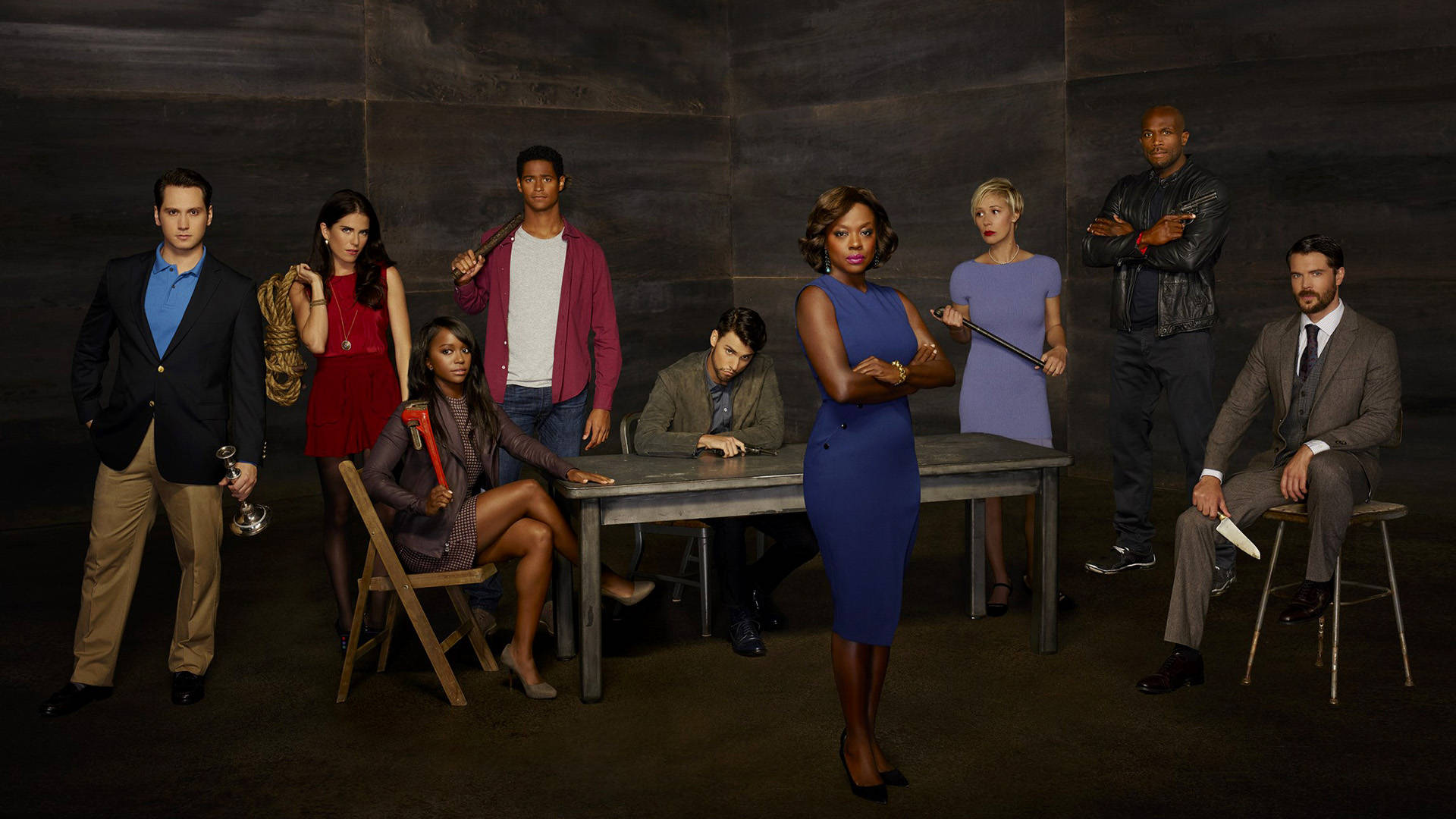 How To Get Away With Murder 桌布 壁紙 — 八位演員在昏暗的房間裡圍著一張木桌戲劇性地擺姿勢，手持各種武器。