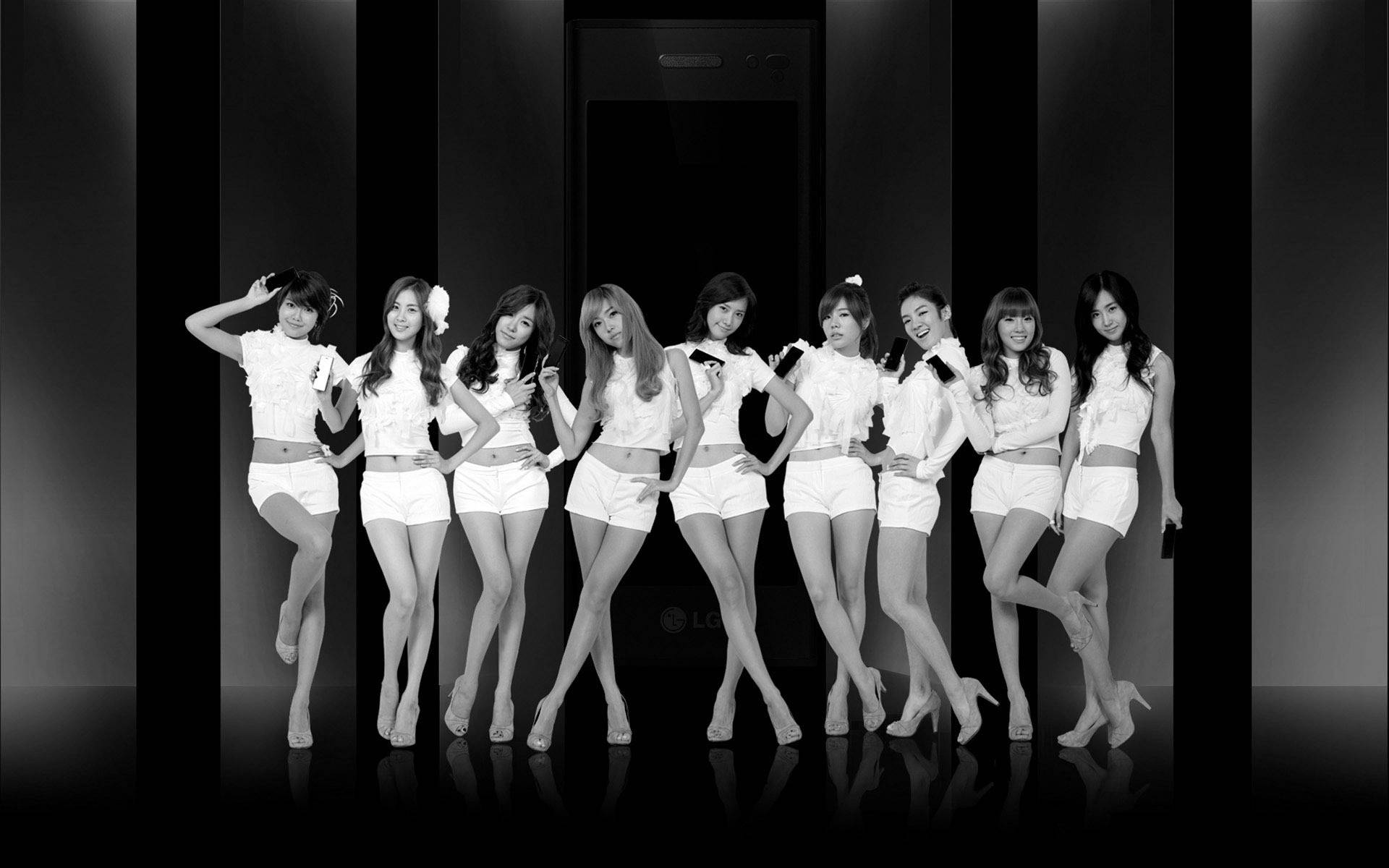 girls 桌布 壁紙 — 八位身穿白色服裝的女性在時尚的黑白工作室中自信地站在巨型電話前擺姿勢。