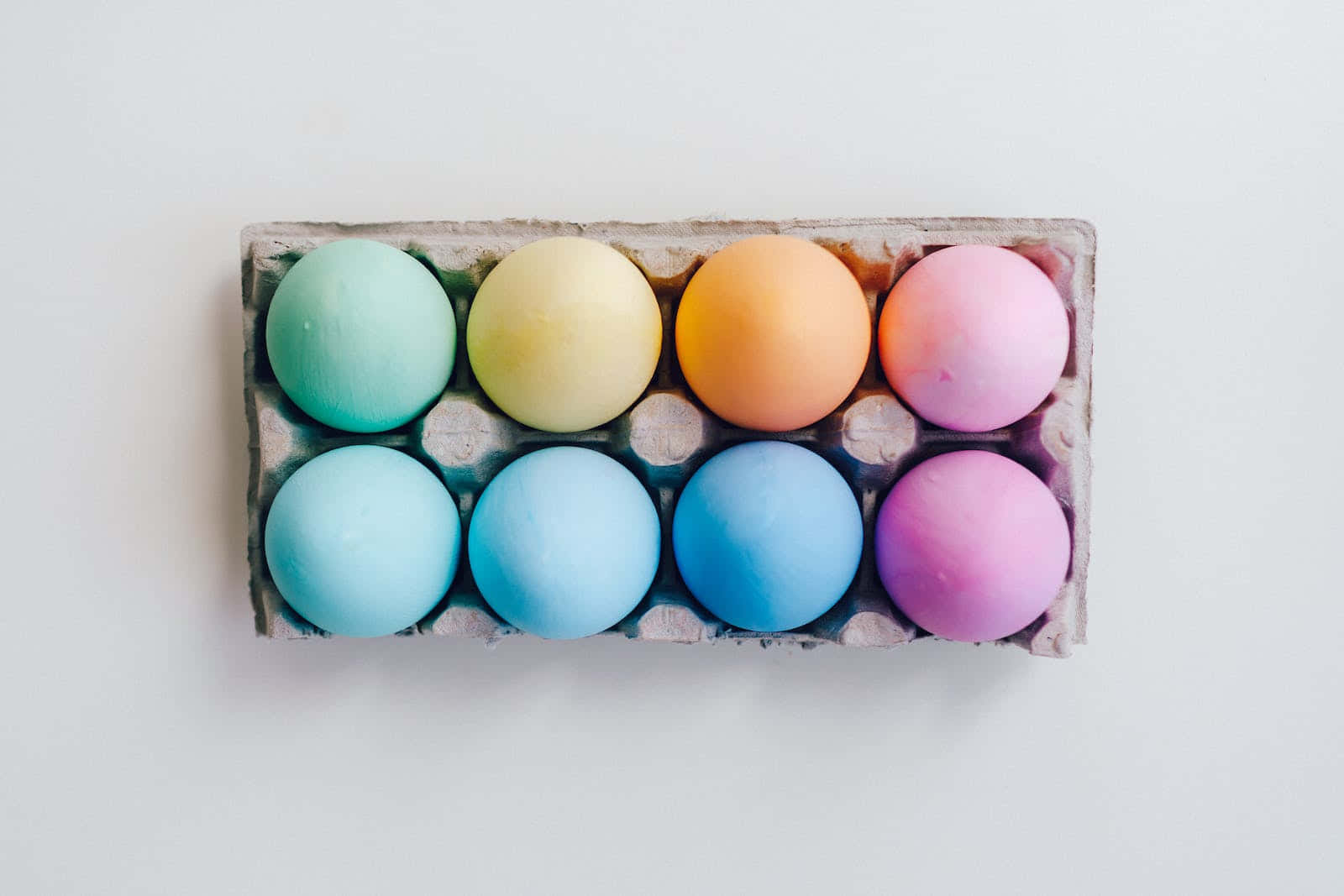 Pastel Easter 桌布 壁紙 — 八個粉彩雞蛋放在紙板托盤中，背景為純白色。