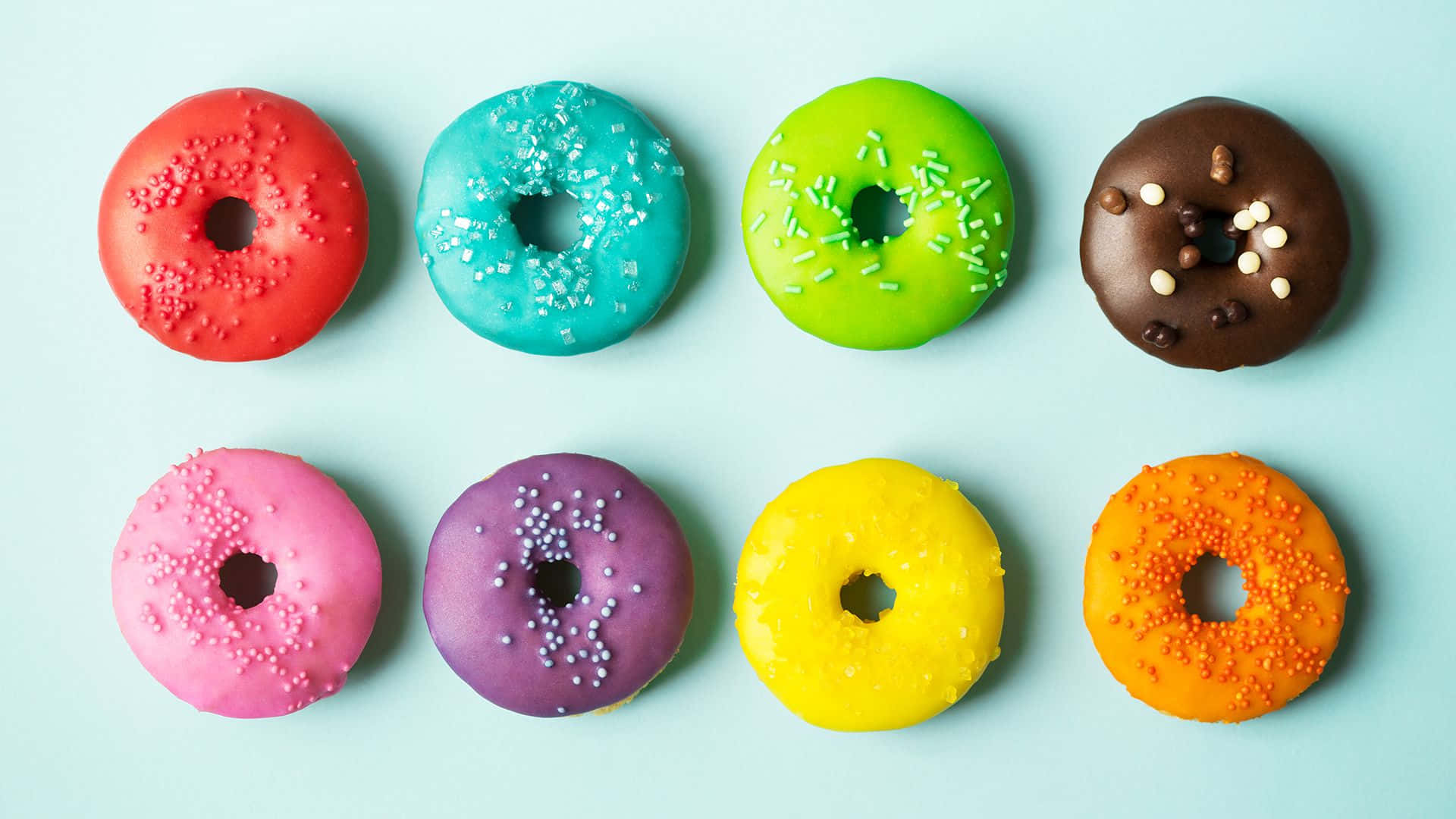 Cute Donut 桌布 壁紙 — 八個色彩鮮豔的糖霜甜甜圈，上面灑滿彩色糖針，整齊排列在柔和的藍色背景上。