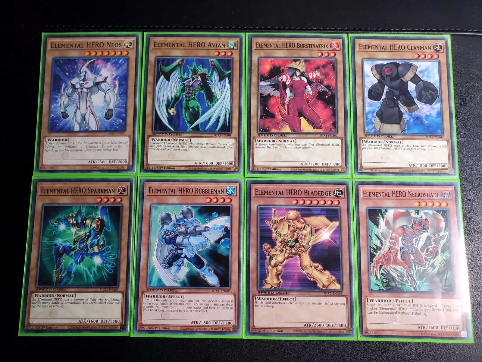 Yugioh Elemental Hero 桌布 壁紙 — 八張遊戲王！元素英雄集換式卡牌在黑色皮革表面上排列成兩行。