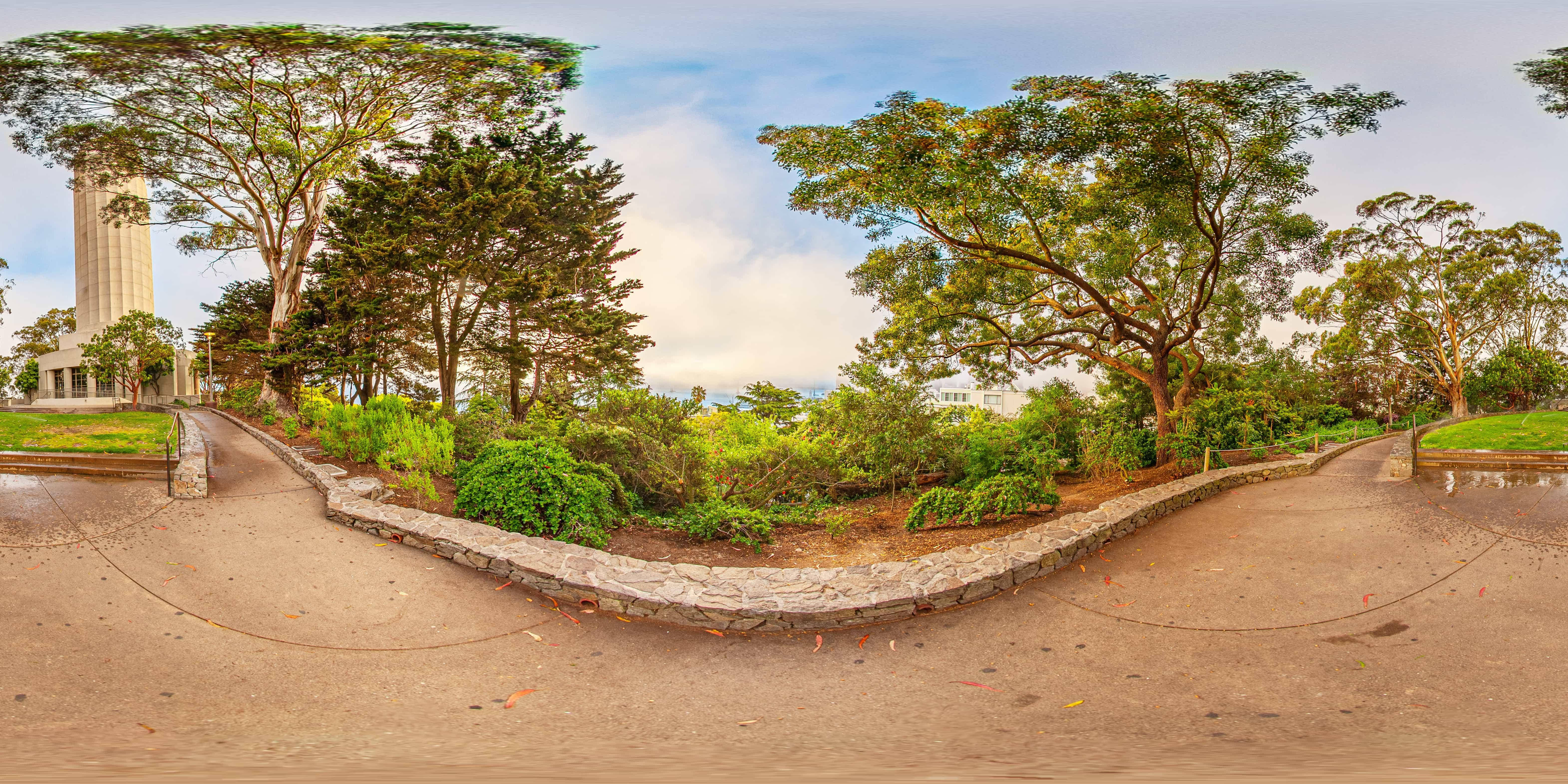 樹木 桌布 壁紙 — 公園全景，蜿蜒的石徑兩旁綠樹成蔭，灌木叢生，天空多雲。
