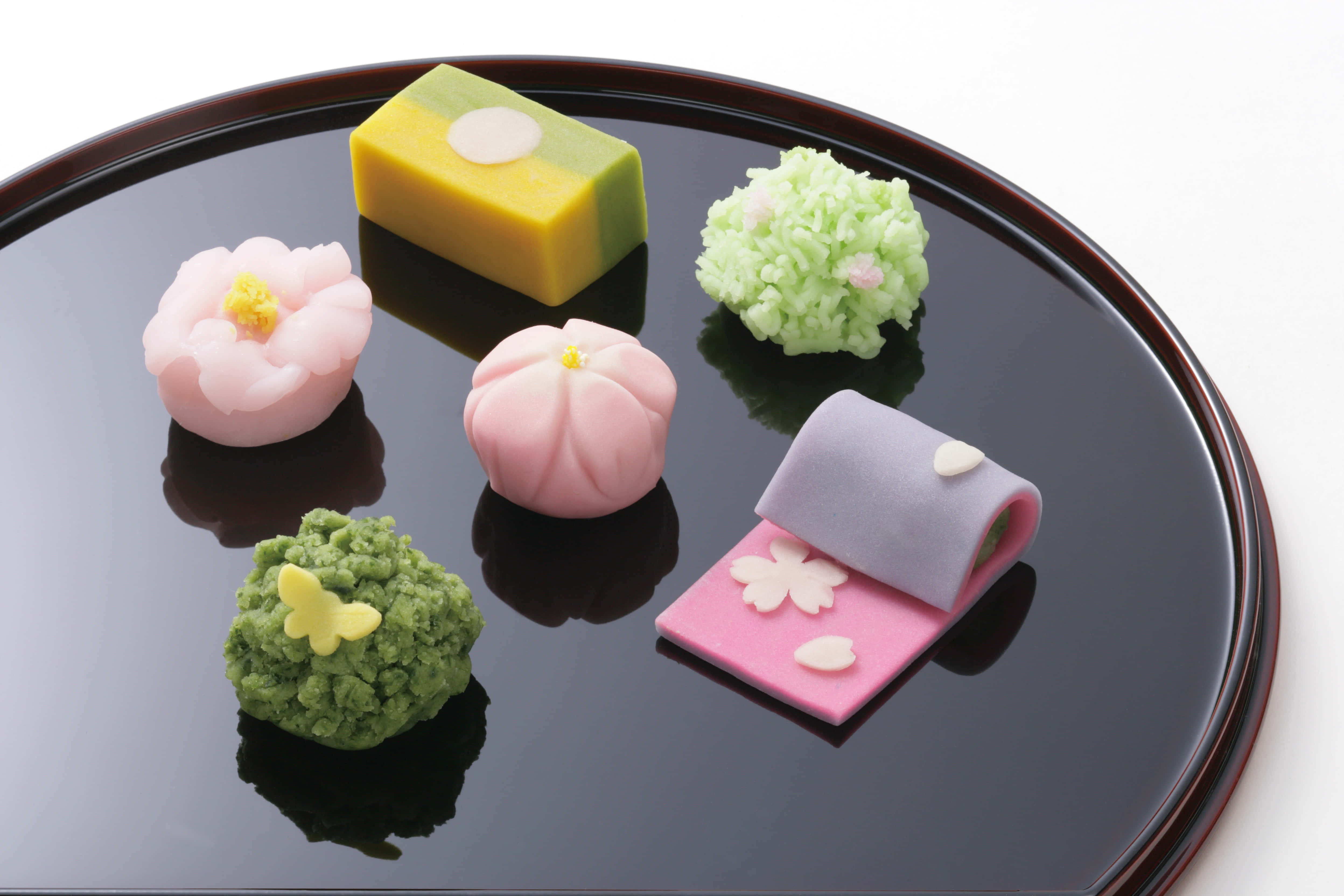 Japanese Sweets 桌布 壁紙 — 六件精緻的日式花形和卷形和菓子放在光亮的黑色漆盤上。