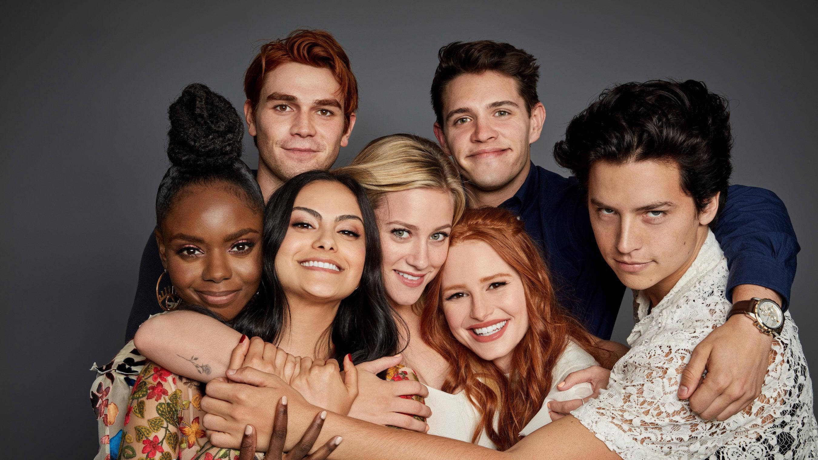 Riverdale 桌布 壁紙 — 六位不同背景的年輕人在柔和燈光的灰色簡約工作室背景下熱情擁抱。