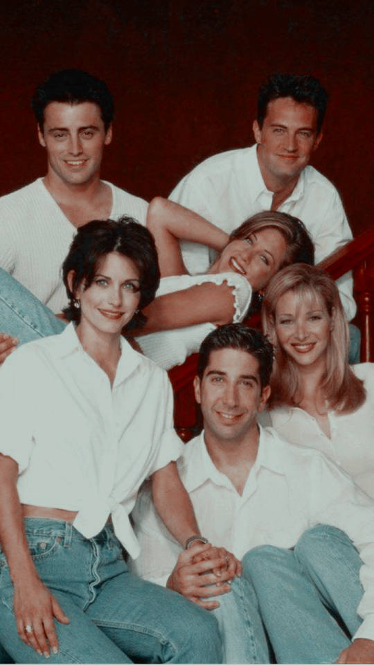 friends tv 桌布 壁紙 — 六位微笑的朋友穿著白襯衫和牛仔褲，在深紅色牆壁前的紅色樓梯上一起擺姿勢。
