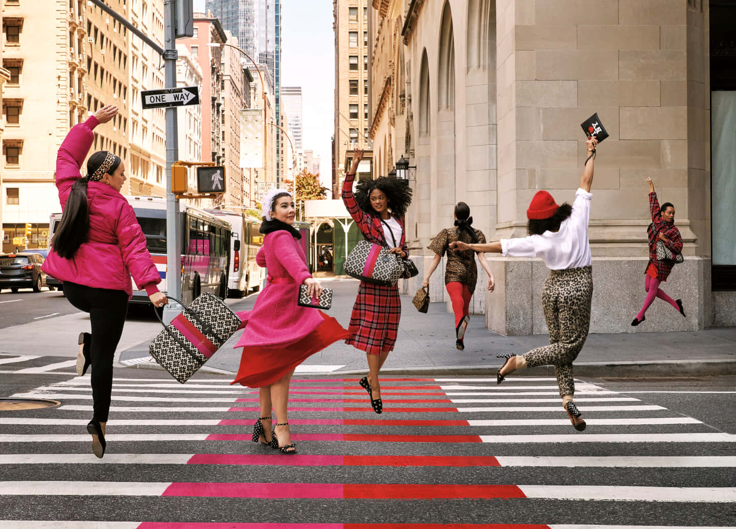 Kate Spade 桌布 壁紙 — 六位時尚女性在繁華的城市街道上，歡快地跳過一條充滿活力的粉紅和白色條紋斑馬線。
