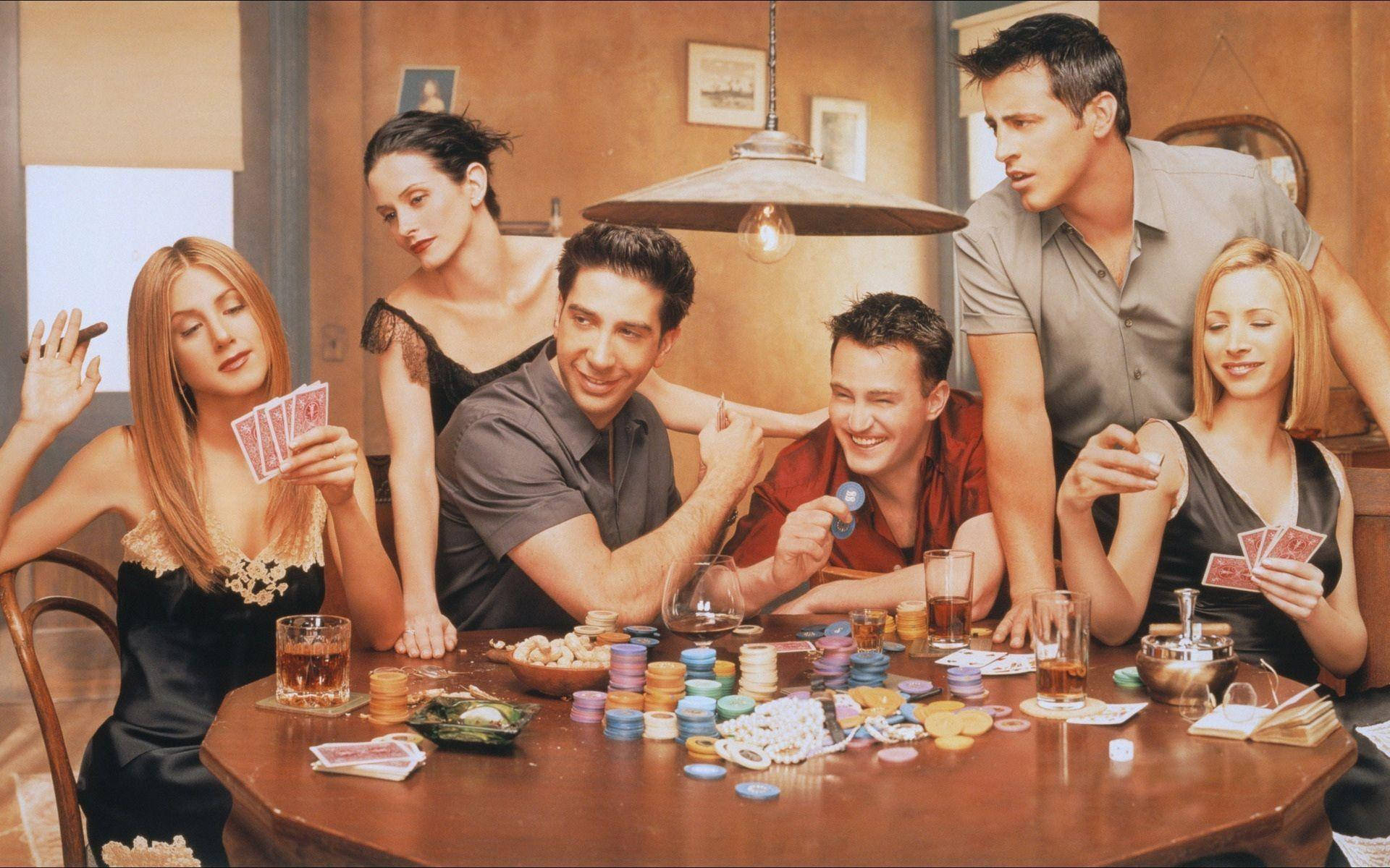 Friends Aesthetic 桌布 壁紙 — 六位朋友圍坐在一間燈光溫暖的公寓裡的木桌旁，投入一場激烈的撲克遊戲，桌上擺滿了色彩繽紛的籌碼和紙牌。
