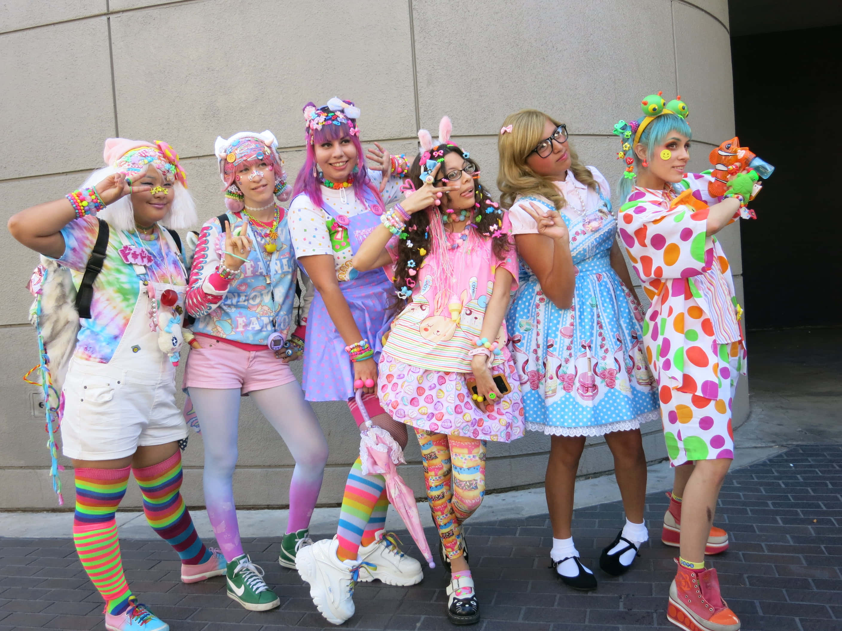 Harajuku Fashion 桌布 壁紙 — 六位朋友穿著色彩繽紛的粉彩服裝和彩虹配飾，在樸素的城牆前開心地擺姿勢。