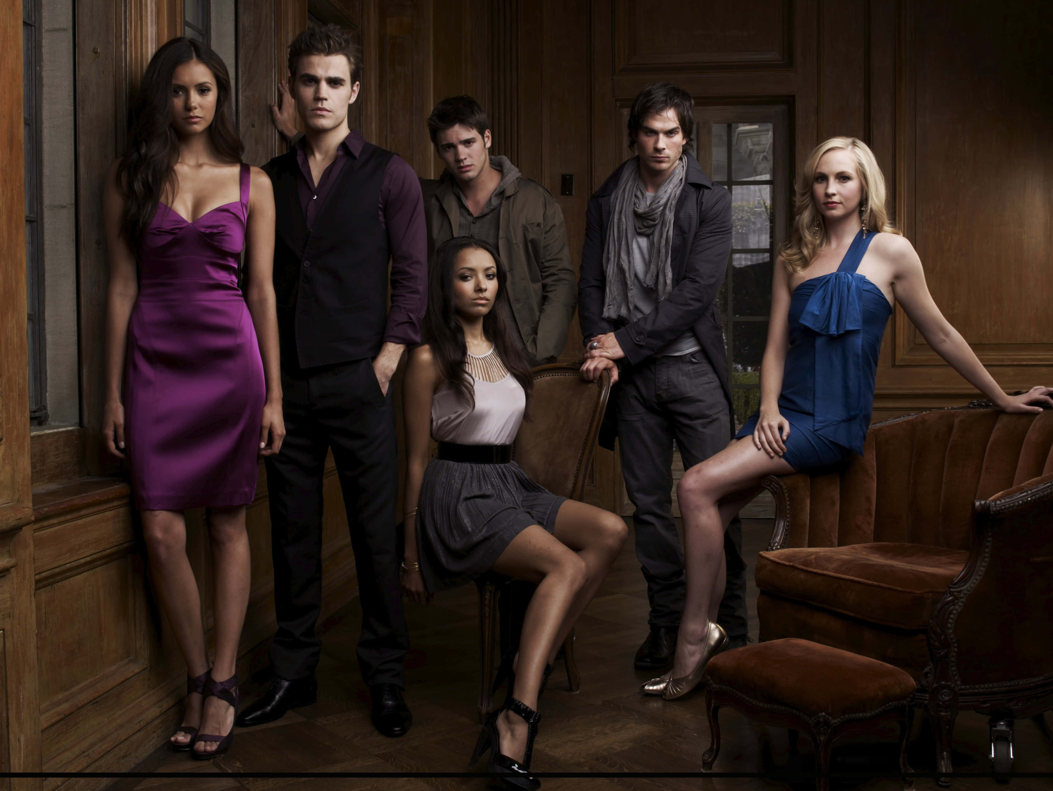 Vampire Diaries Desktop 桌布 壁紙 — 六位演員穿著時尚晚裝，在一個裝飾華麗的木質鑲板房間內，配以復古家具，戲劇性地擺出姿勢。