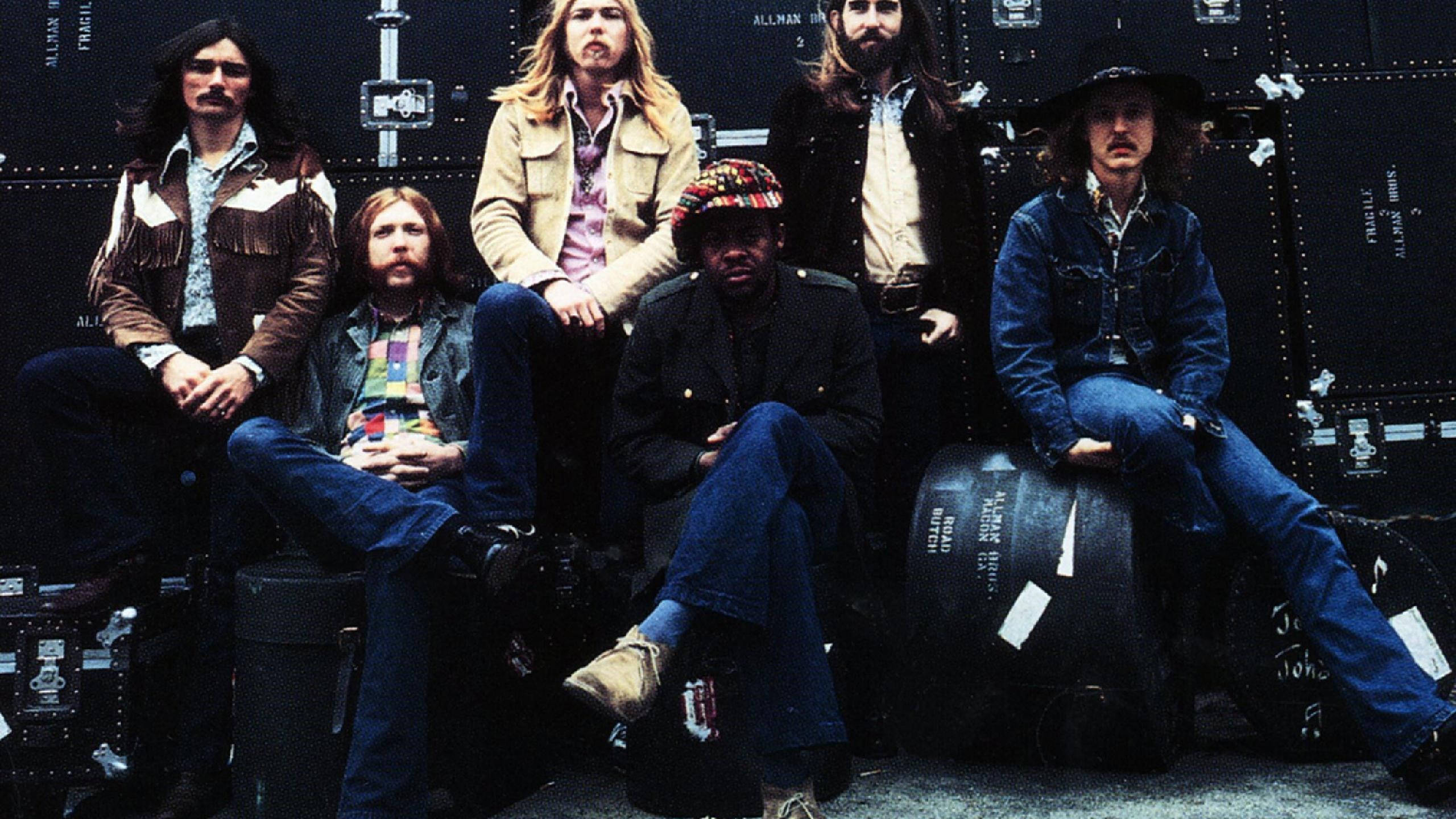 音樂 桌布 壁紙 — 六位身穿1970年代搖滾服飾的音樂人，在黑暗的巡迴巴士背景下，隨意地坐在設備箱上擺姿勢。