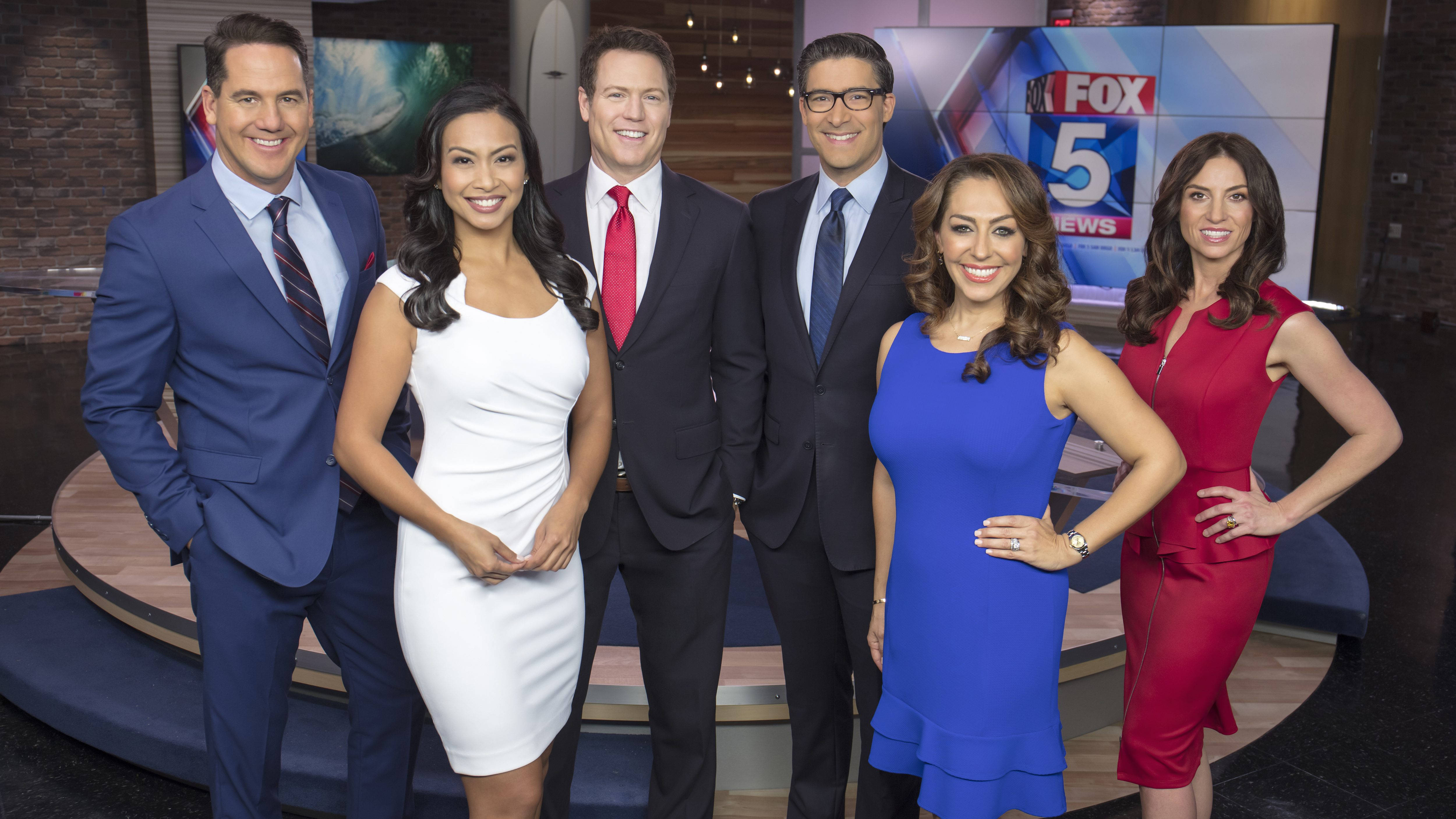 News 桌布 壁紙 — 六位面帶微笑的新聞主播身著正裝，在設有FOX 5 News背景的現代電視攝影棚中自信地擺姿勢。