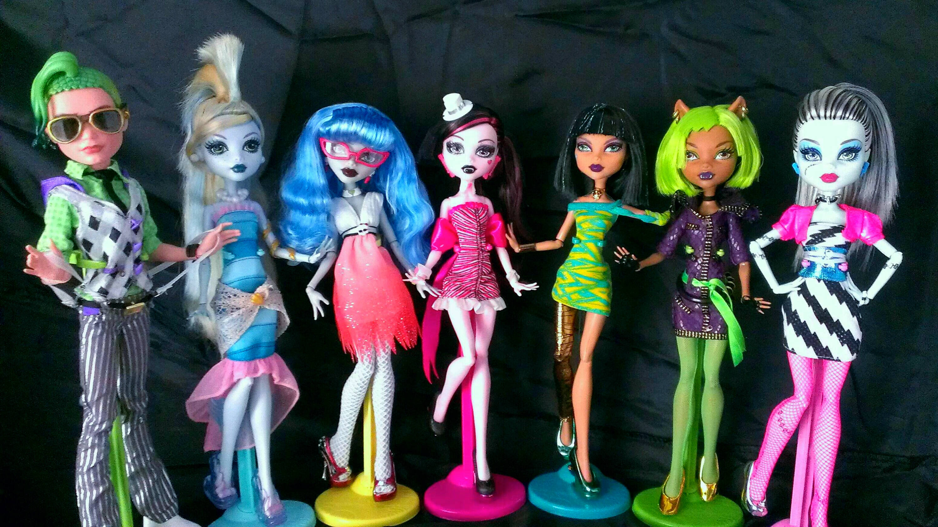 bratz 美學 桌布 壁紙 — 六個Monster High公仔穿著色彩繽紛的服裝，在黑色背景前的彩虹架上擺姿勢。