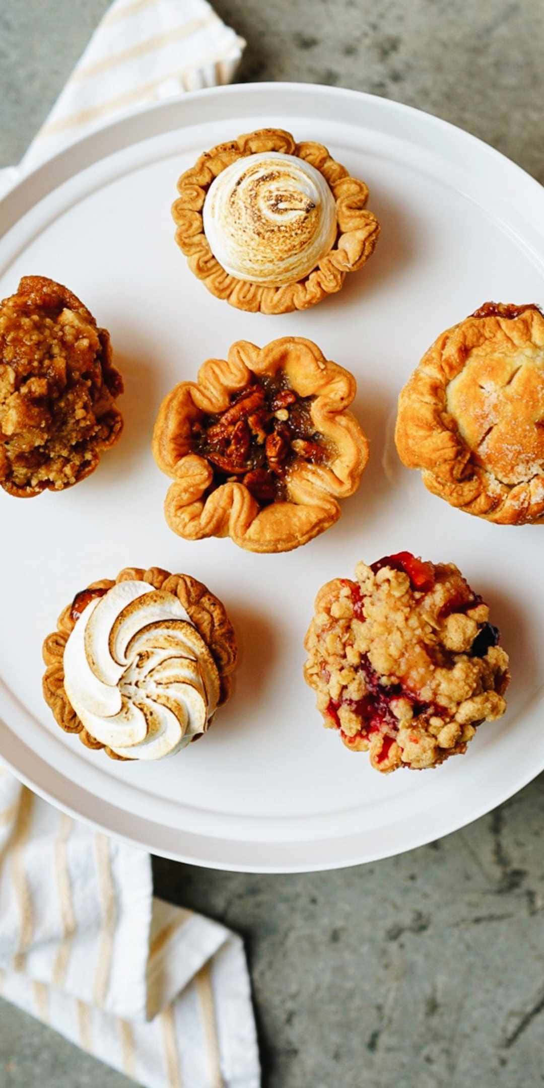 Pie 桌布 壁紙 — 六個各式各樣的金黃色迷你派，上面有蛋白霜烤核桃和雜莓金寶，放在白色盤子上。