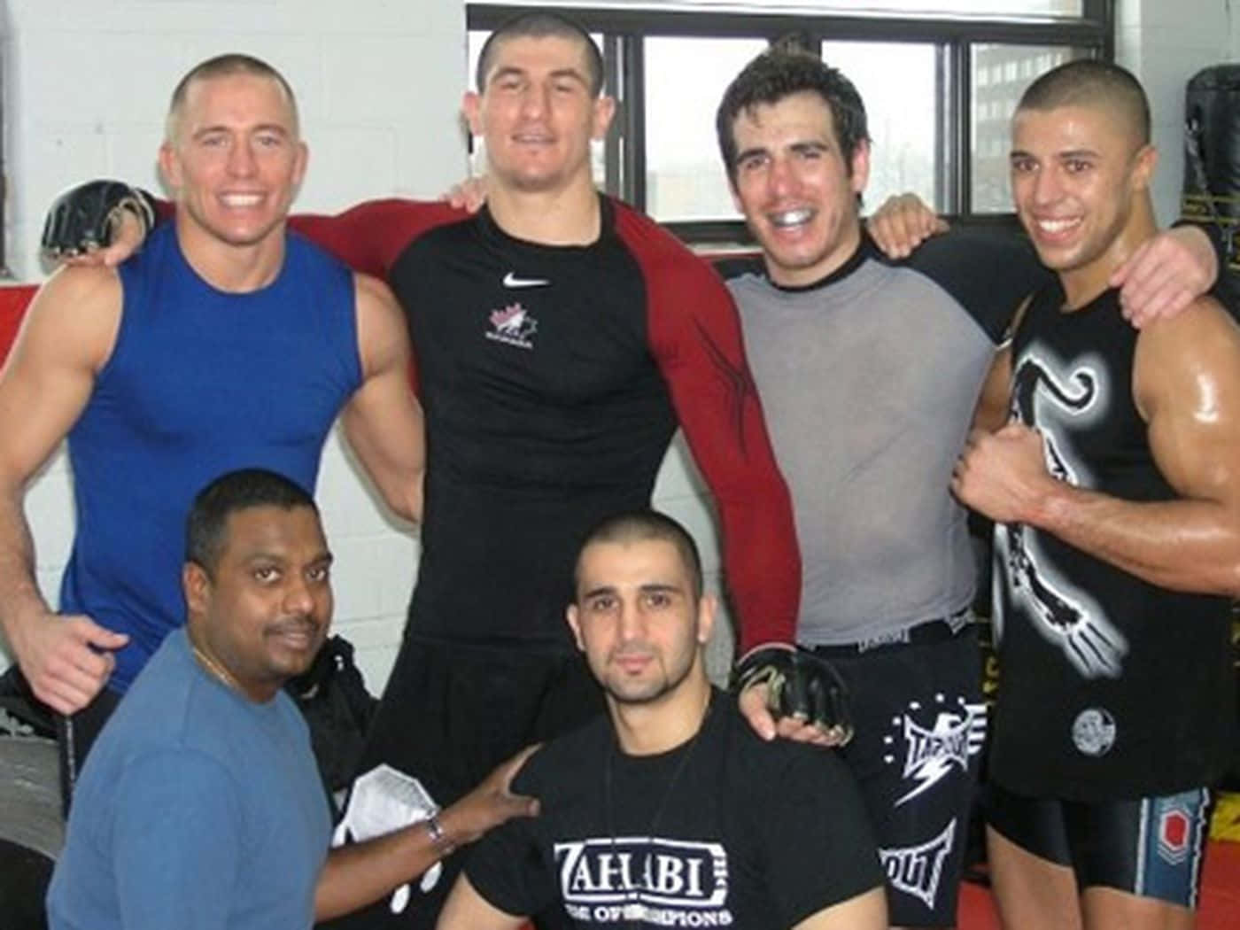 UFC 桌布 壁紙 — 六個微笑的肌肉男穿著健身服裝，在明亮的訓練設施中互相搭肩合照。