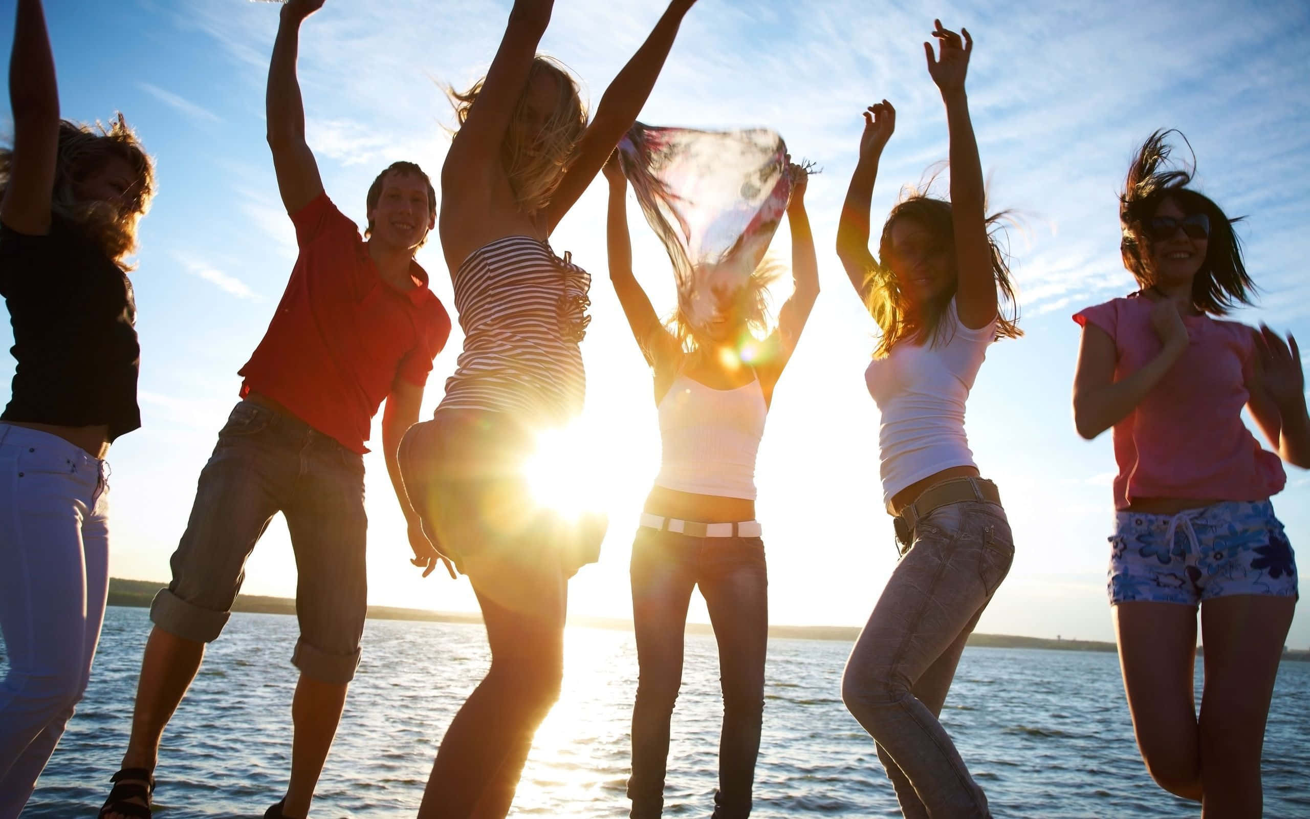 Beach Dance Party 桌布 壁紙 — 六個快樂的朋友在金色日落、陽光閃耀和風吹亂髮的海灘上跳躍起舞。