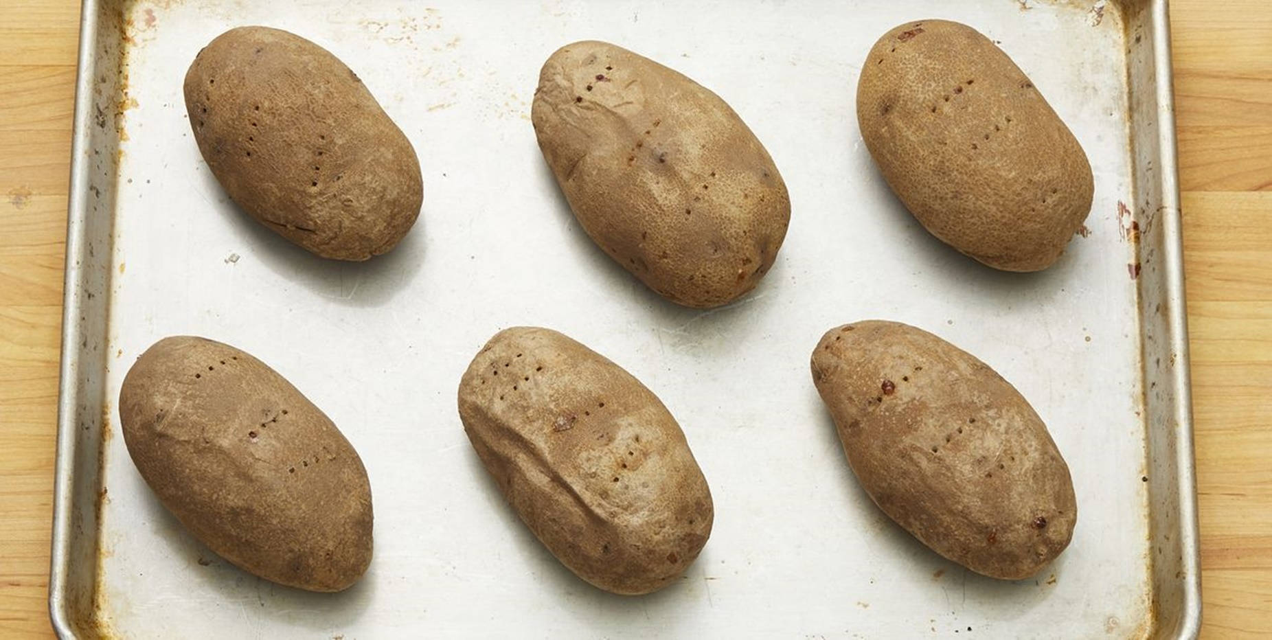 Potato 桌布 壁紙 — 六個未剝皮的棕色馬鈴薯排列在一個用過的金屬烤盤上，放在木質表面上。