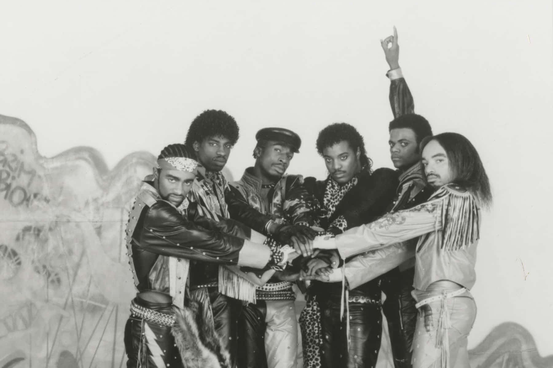 黑白 桌布 壁紙 — 六個穿著大膽1980年代時尚的男人，在一個引人注目的黑白照片中，緊密相連地對著塗鴉牆擺姿勢。