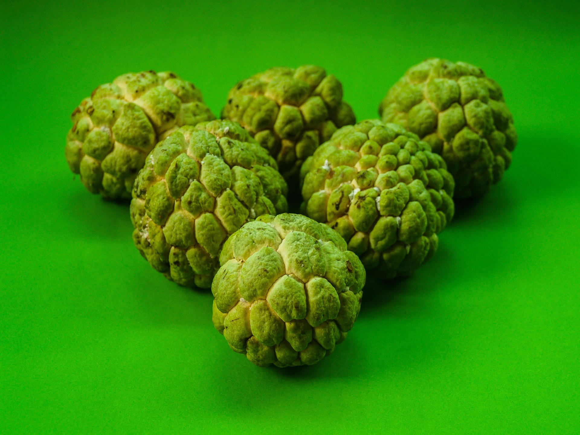 Fruit 桌布 壁紙 — 六個綠色的牛油果蘋果，表面凹凸不平，排列在充滿活力的純綠色背景上。