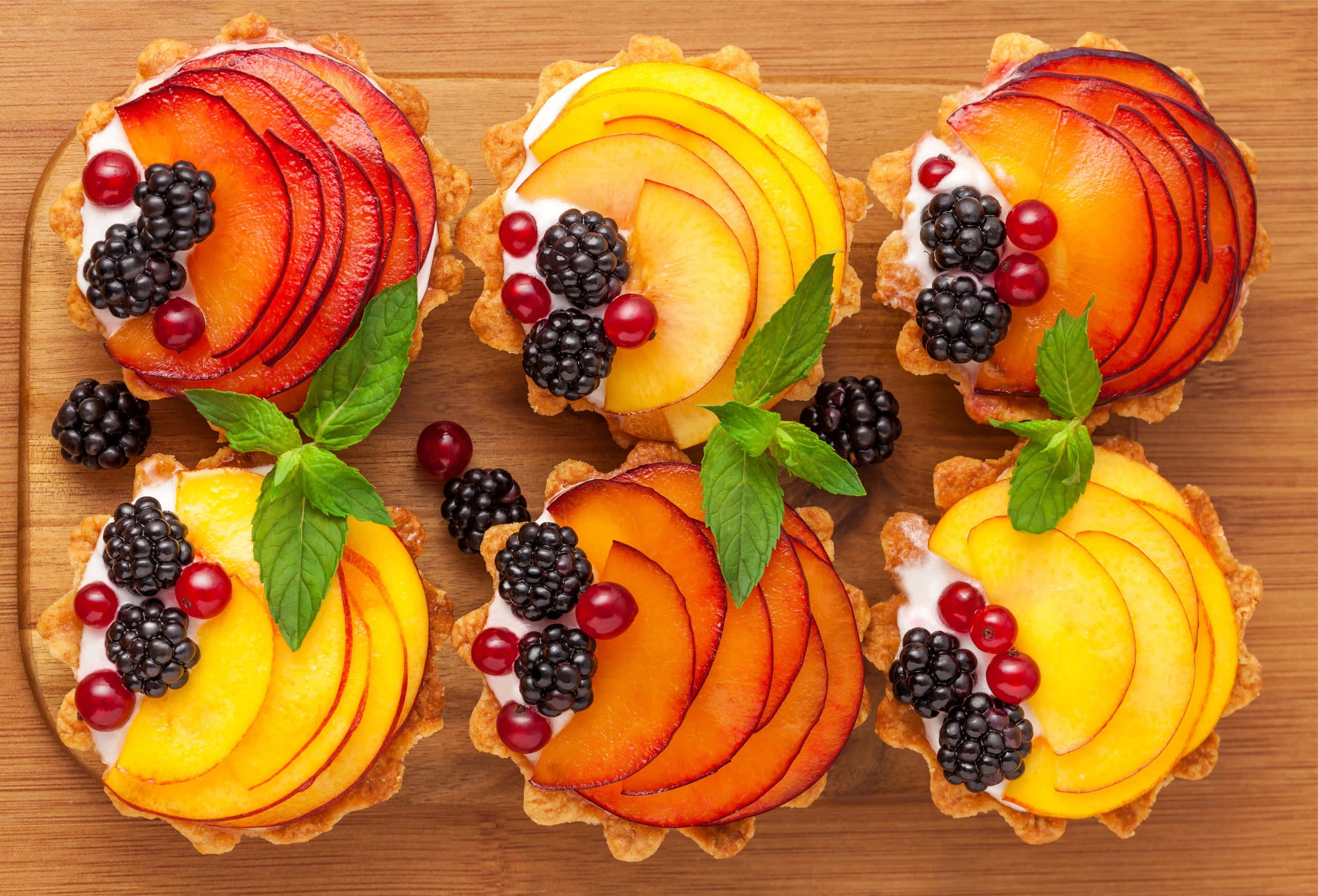 Spring Desserts 桌布 壁紙 — 六個色彩繽紛的水果塔，上面放有桃子片、黑莓和紅醋栗，排列在木板上。