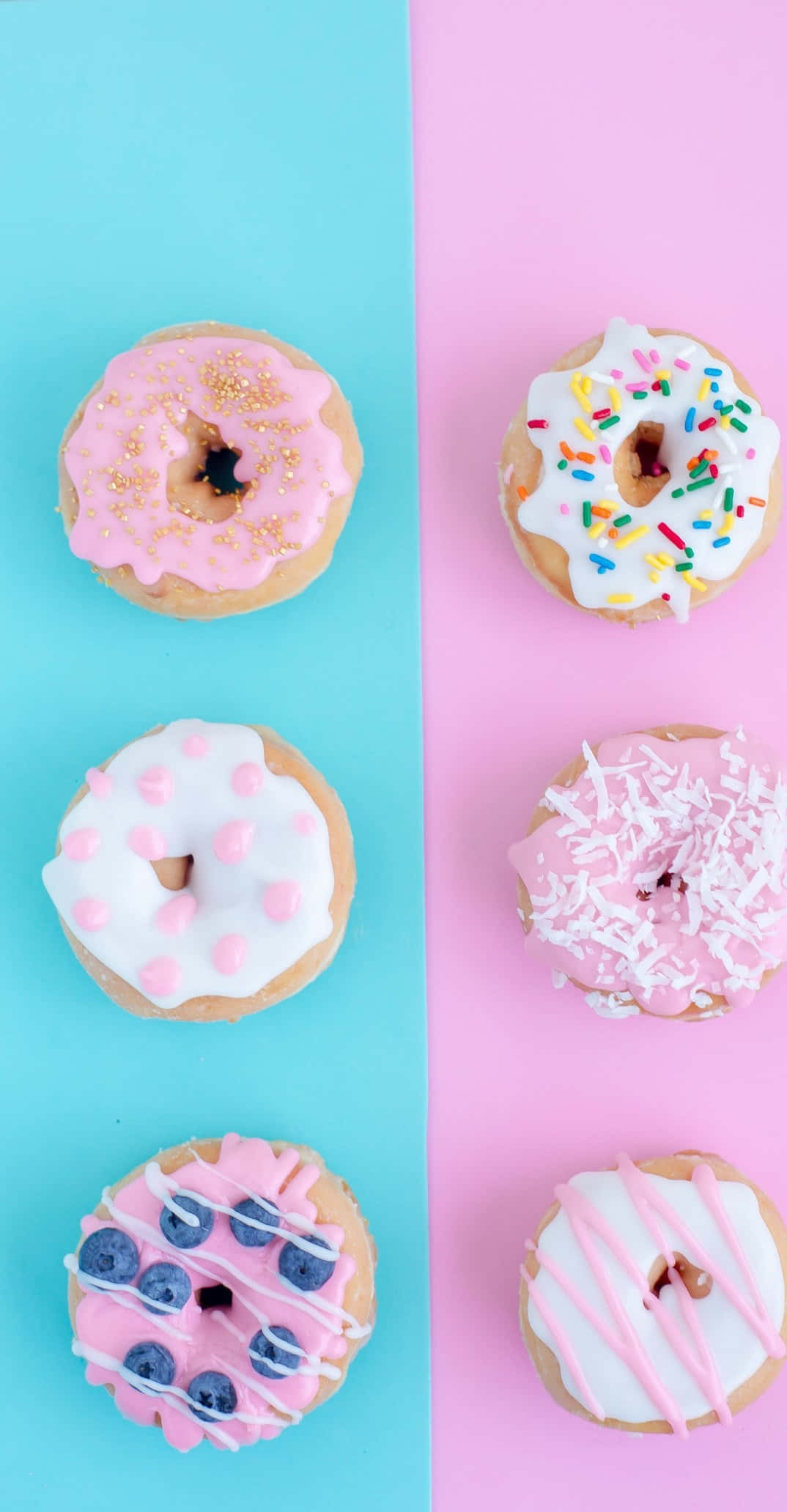 Pixel 3 Desserts 桌布 壁紙 — 六個色彩繽紛的糖霜甜甜圈，上面有彩色糖粒和藍莓，排列在粉紅和藍色分割的背景上。
