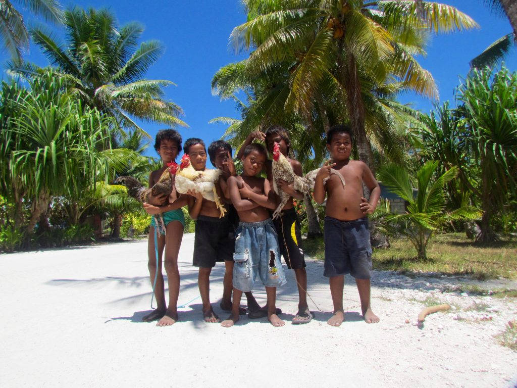 Kiribati 桌布 壁紙 — 六個赤腳的孩子在陽光普照的沙路上，在搖曳的棕櫚樹下自豪地抱著雞。