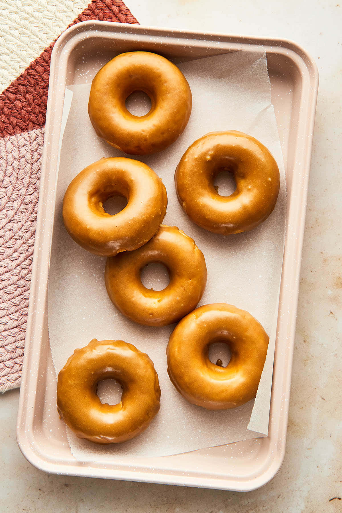 Glazed Donut 桌布 壁紙 — 六個釉面甜甜圈放在粉紅色托盤的烘焙紙上，旁邊有一塊有紋理的粉白色布。