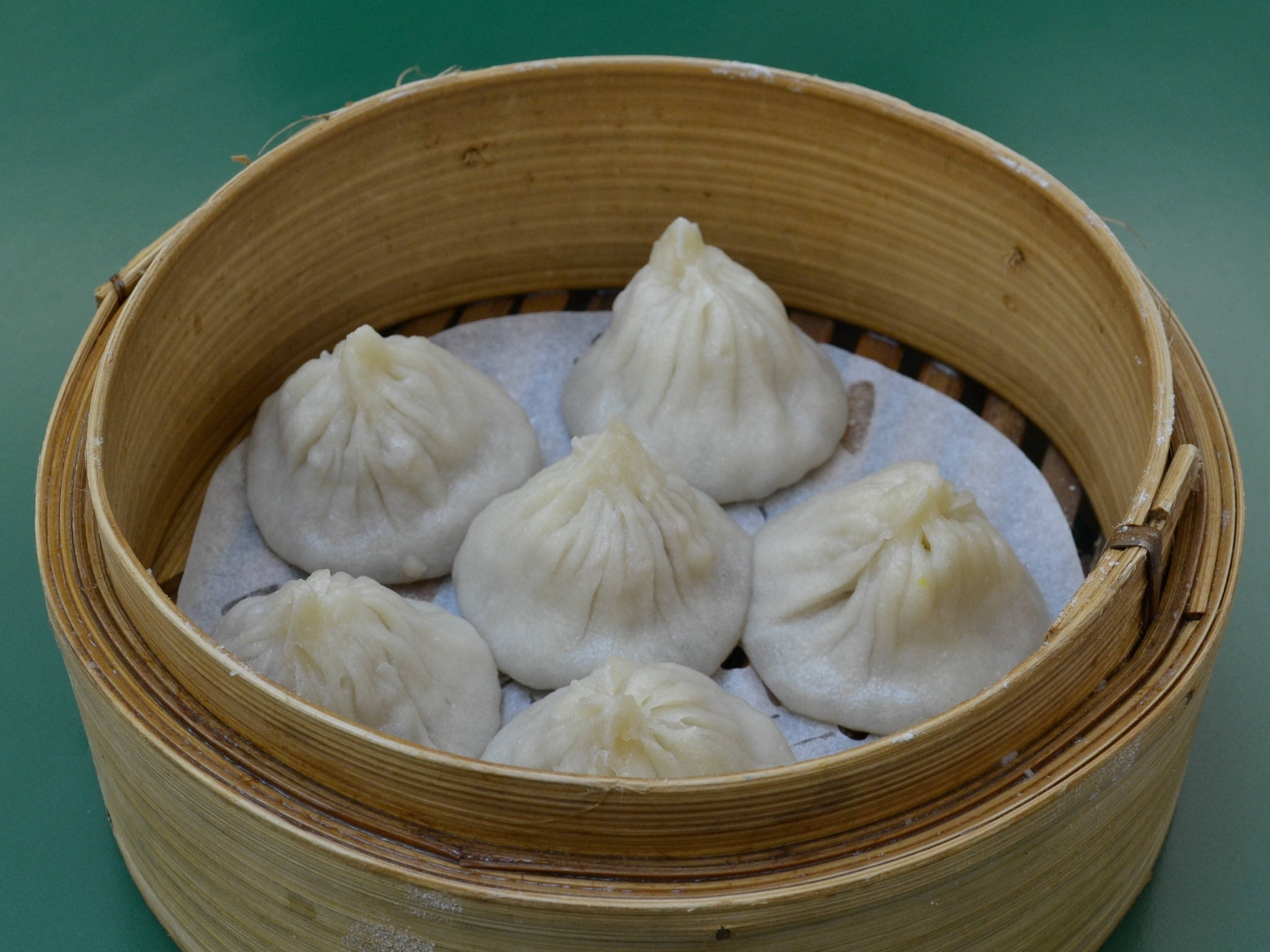 steam 桌布 壁紙 — 六個飽滿的白色餃子，頂部有褶皺，放在綠色表面上的竹蒸籠裡。