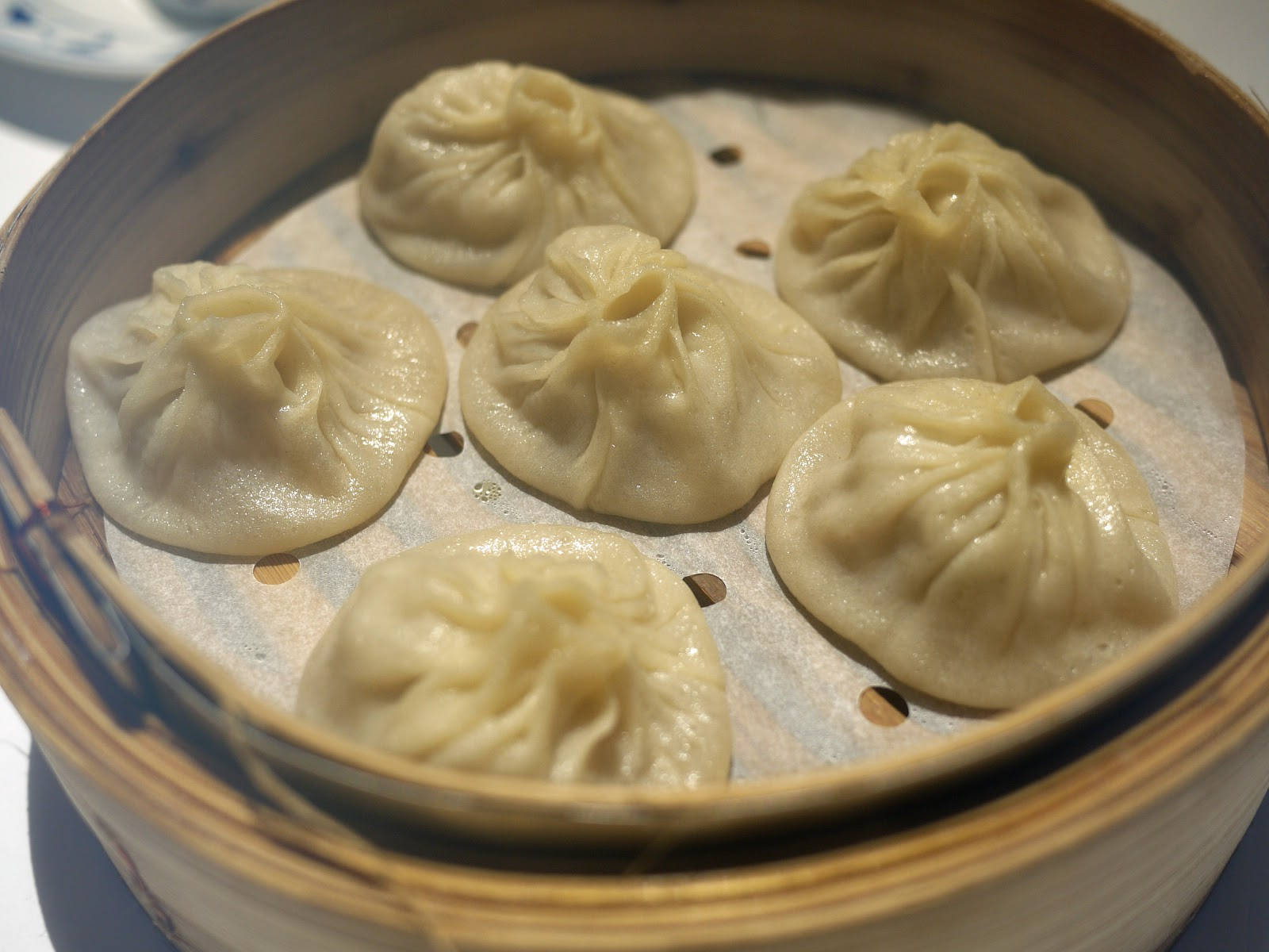steam 桌布 壁紙 — 六個飽滿的蒸餃，頂部有褶皺，放在鋪有烘焙紙的竹蒸籠裡。