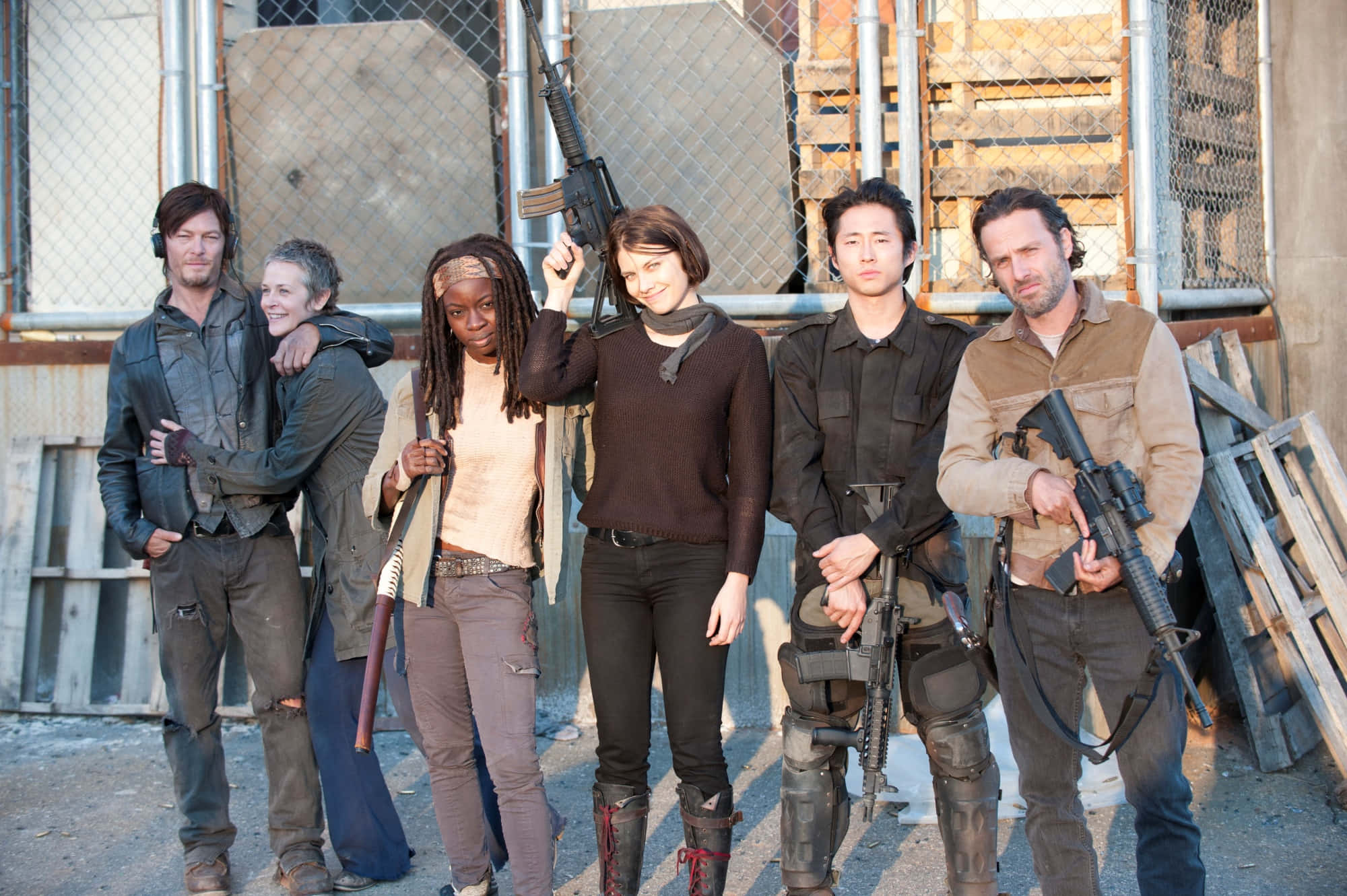 walking dead 桌布 壁紙 — 六名武裝倖存者在明亮的日光下，站在一個骯髒的城市垃圾場中。