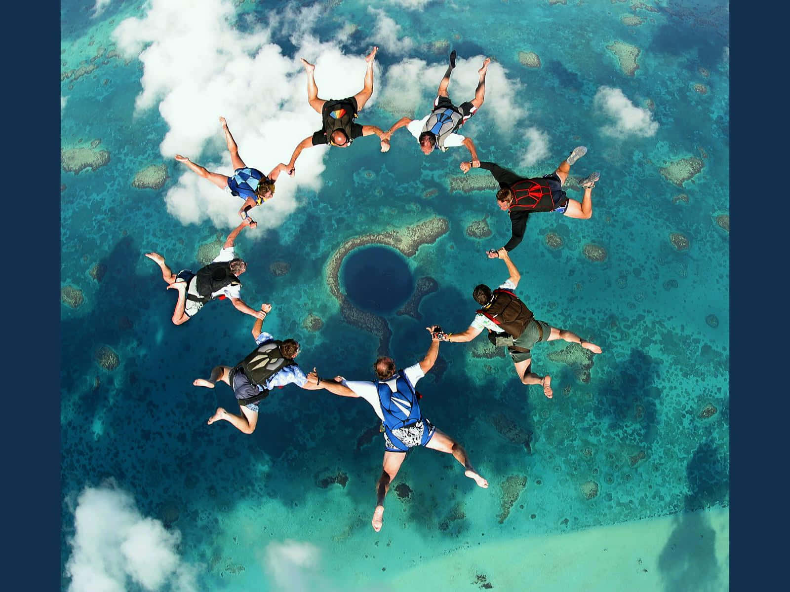 海洋 桌布 壁紙 — 六名跳傘者在空中形成一個圓圈，下方是帶有中央藍色沉洞的碧綠潟湖。