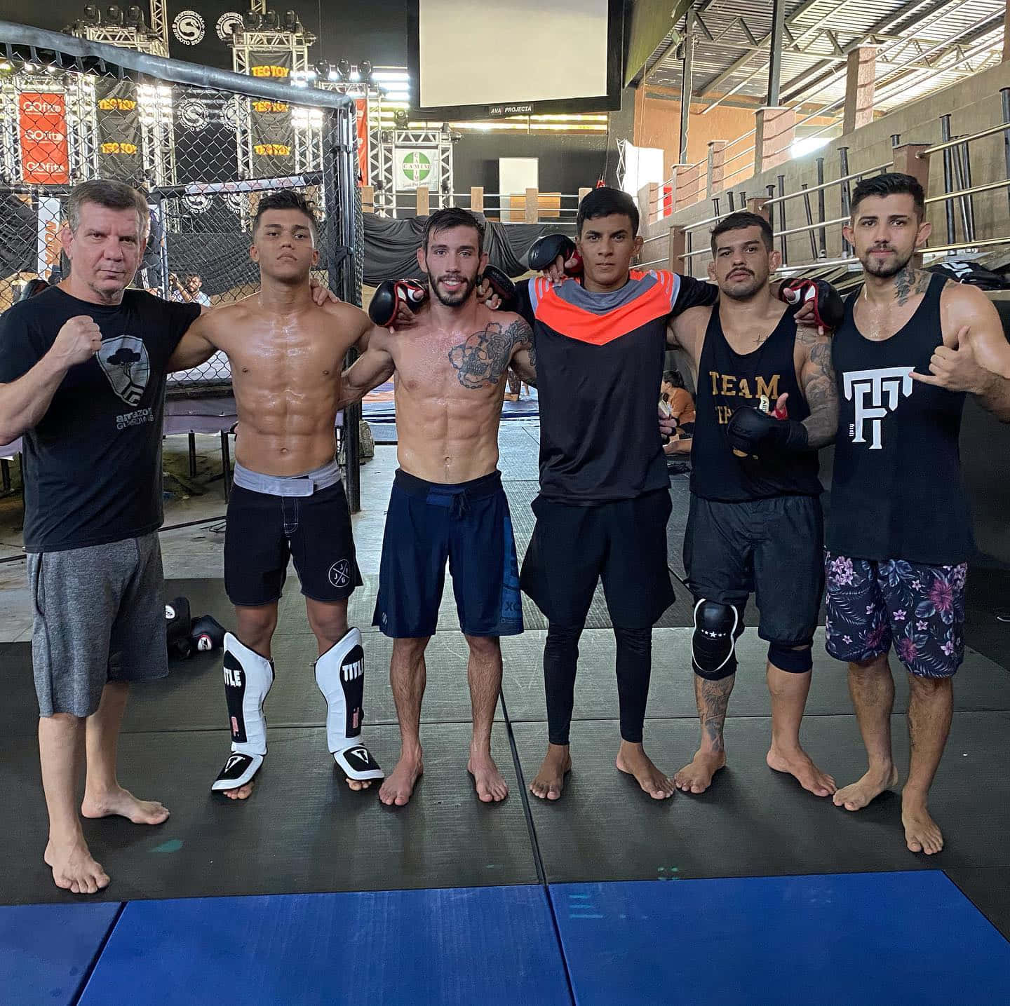 MMA 桌布 壁紙 — 六名身穿戰鬥裝備的男子在設有軟墊和頂燈的MMA籠內自信地擺姿勢。