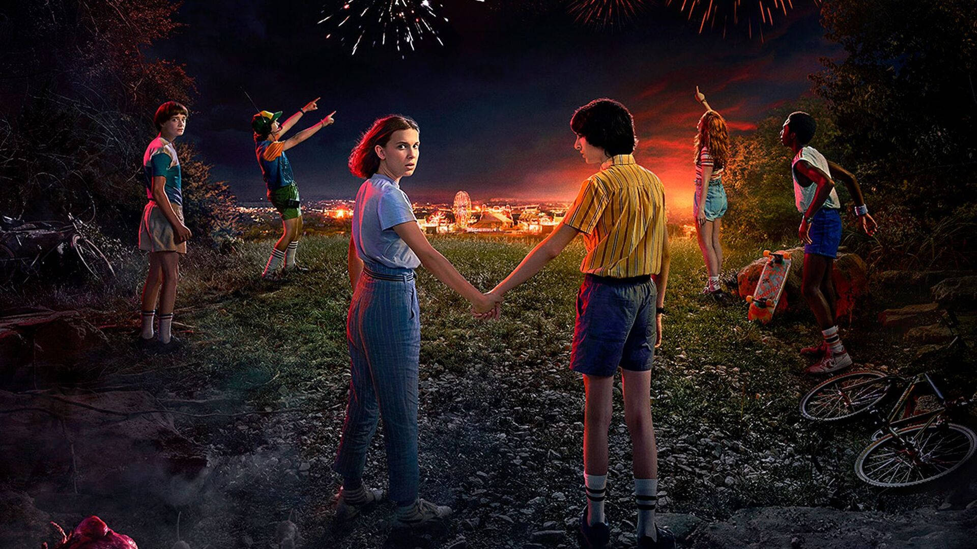 Stranger Things 3 桌布 壁紙 — 六名青少年在黃昏時站在山丘上，手牽著手，煙火在下方閃爍的小鎮上空爆炸。
