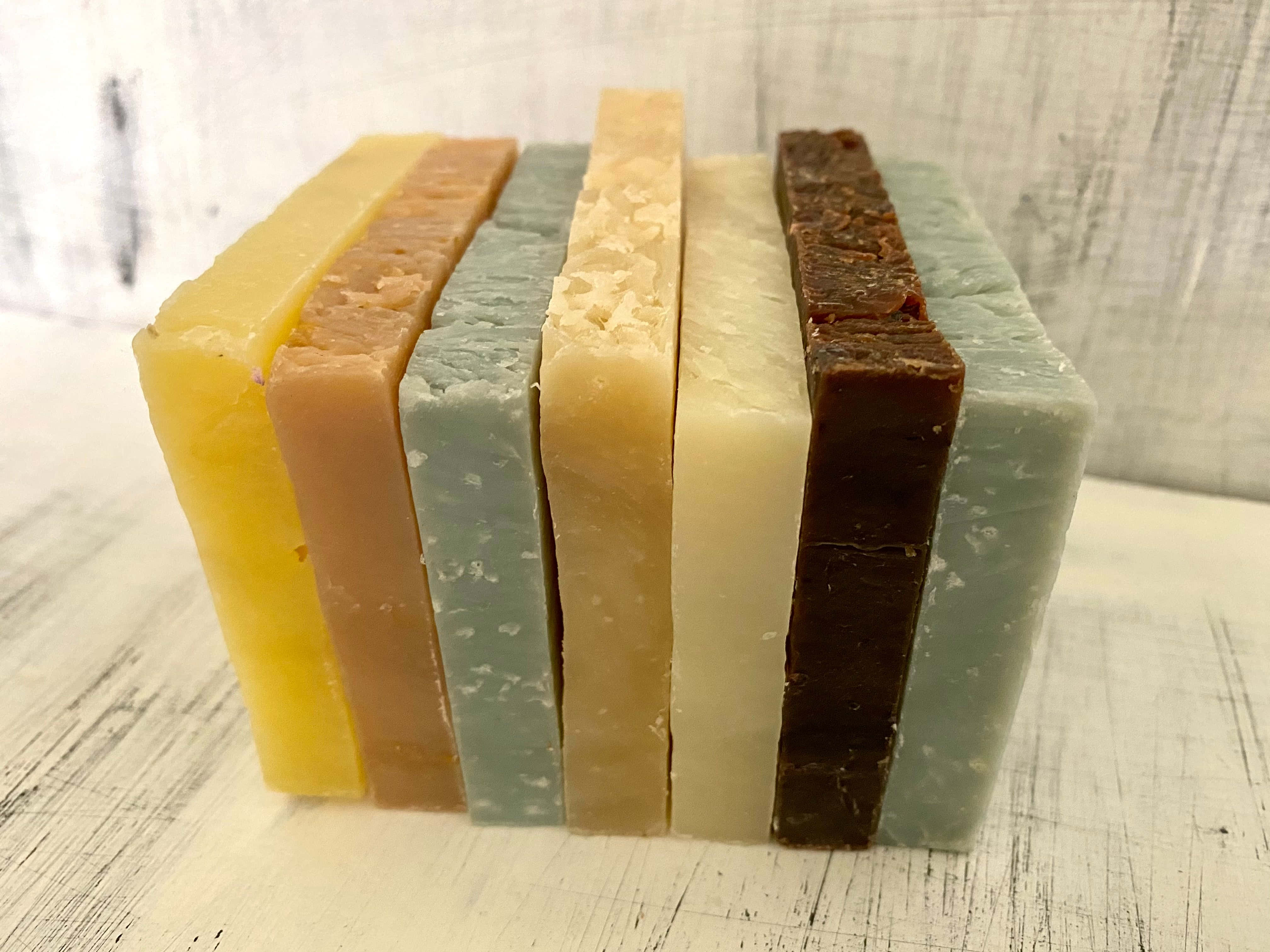 bath 桌布 壁紙 — 六塊手工皂以多種大地色調整齊排列在經風化的白色木質表面上。