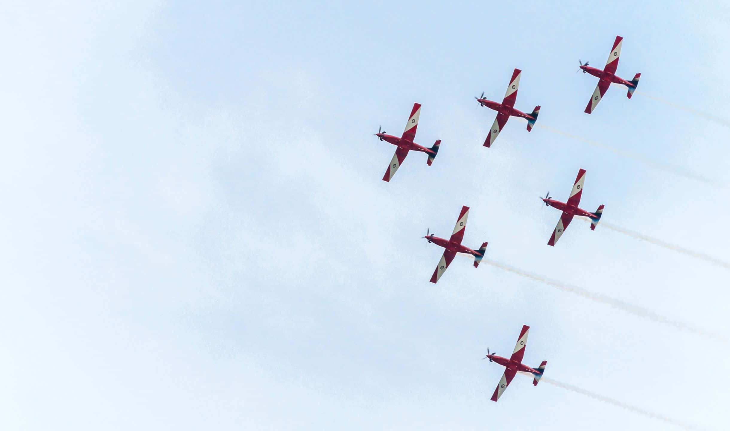 2440x1440 Small Planes 桌布 壁紙 — 六架紅色特技飛機以緊密編隊飛過淡藍色的天空，身後留下白色煙跡。