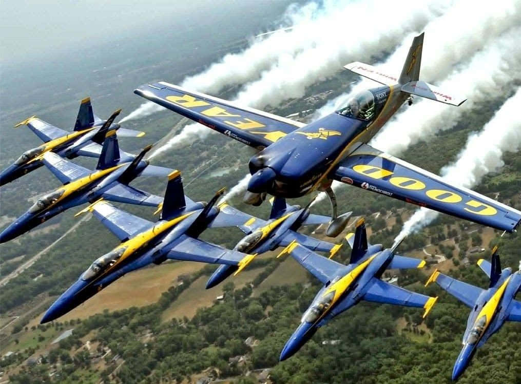 US Navy 桌布 壁紙 — 六架藍天使噴射機以緊密編隊飛過頭頂，在綠色森林景觀上空留下白色煙跡。