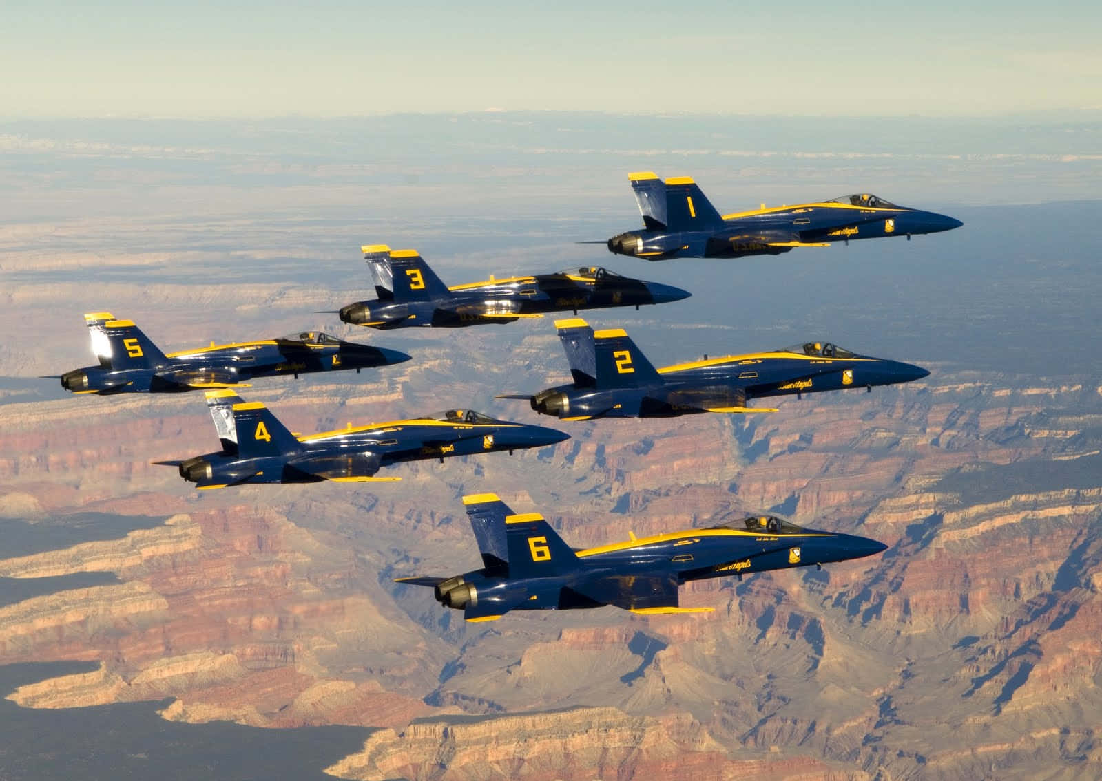 US Navy 桌布 壁紙 — 六架藍黃色戰鬥機在大峽谷廣闊的紅色岩石峽谷上空緊密編隊飛行。