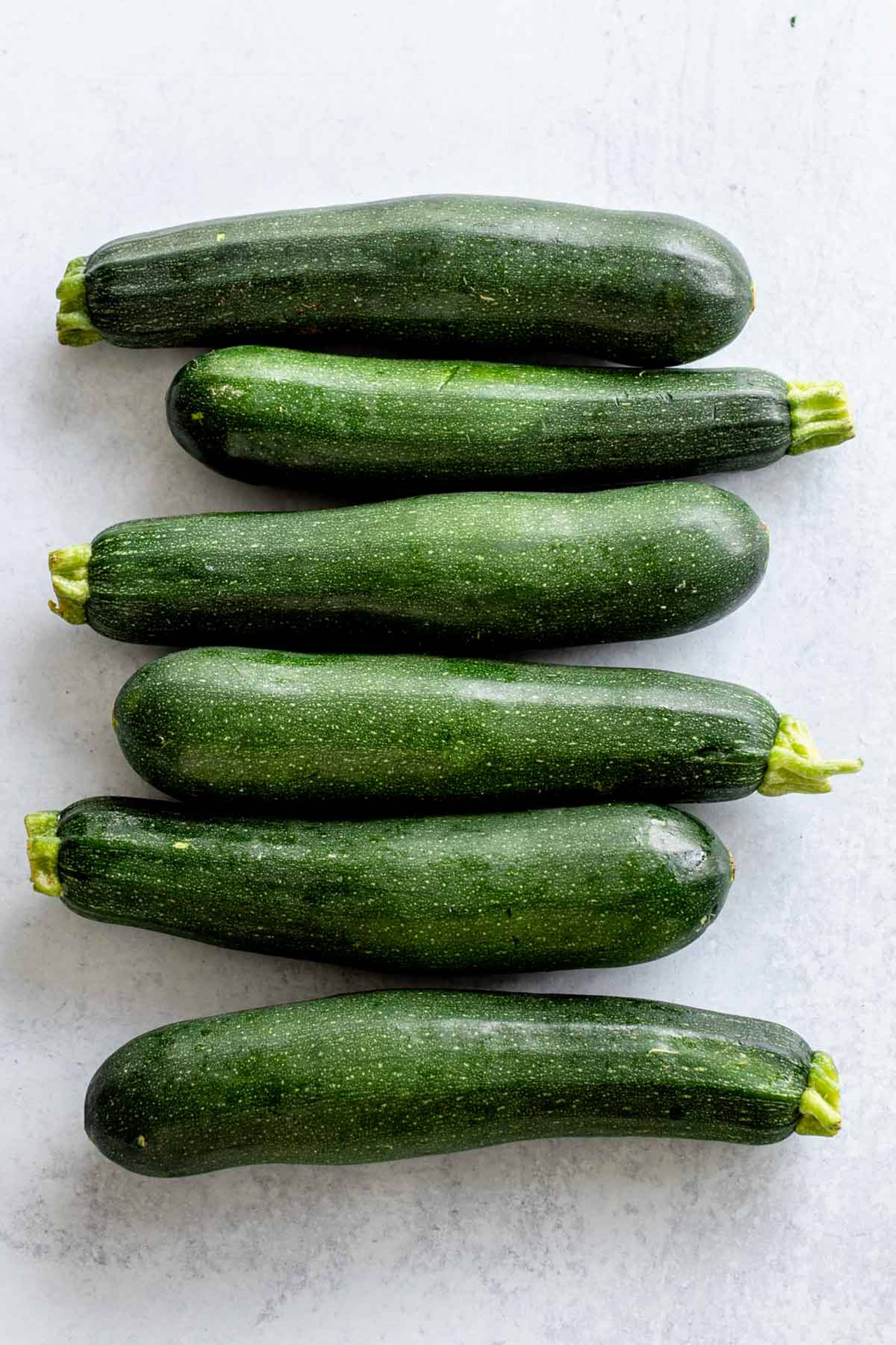 food iPhone 桌布 壁紙 — 六條新鮮的綠色櫛瓜，帶有黃色莖部，對角排列在淺灰色紋理表面上。