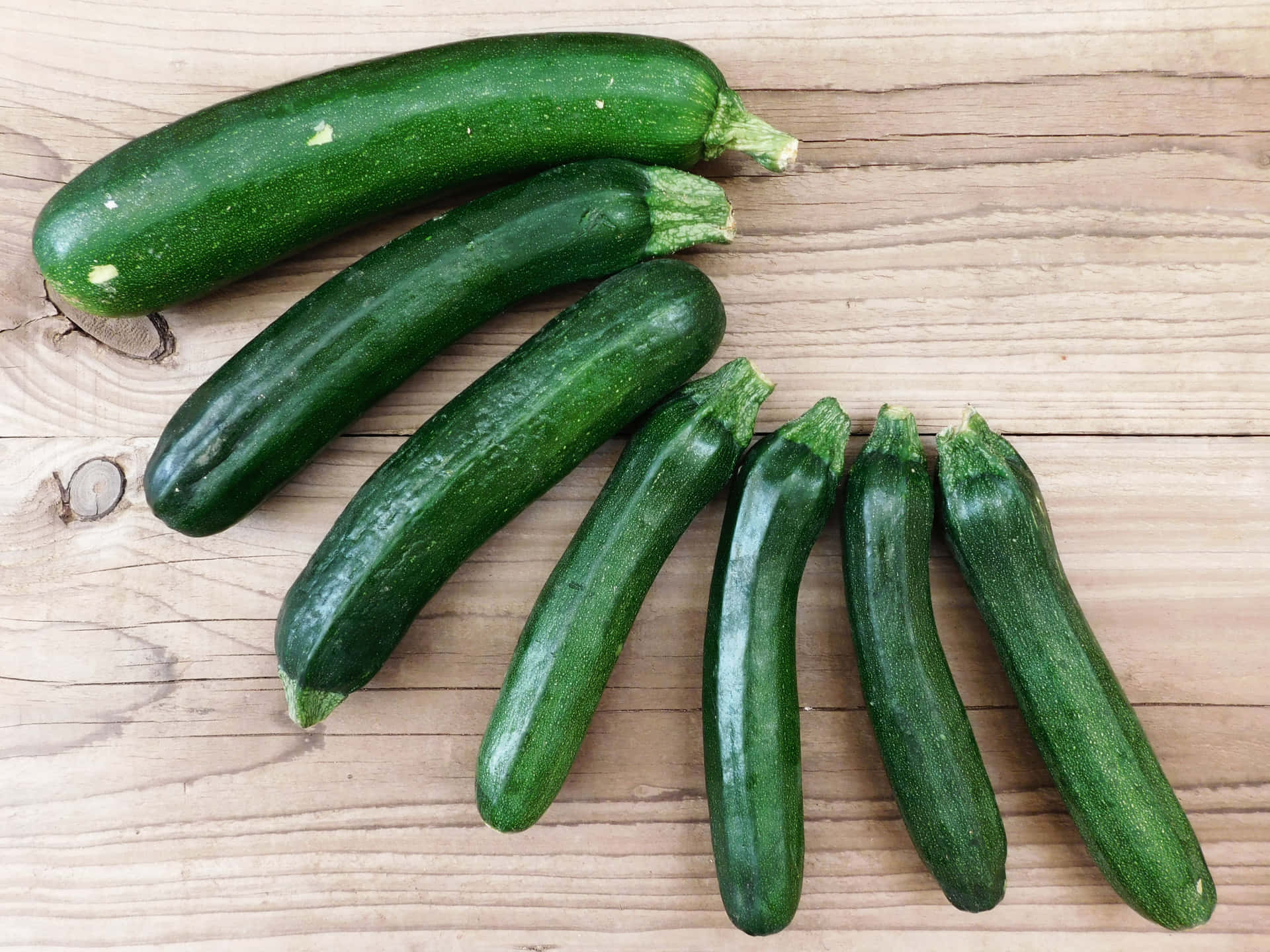 Zuchinis 壁紙 — 六條新鮮的綠色櫛瓜對角排列在淺色木紋表面上。