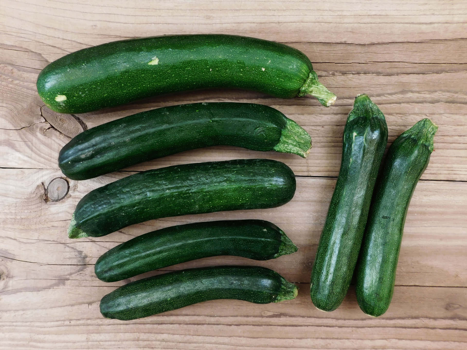Zuchinis 壁紙 — 六條新鮮的綠色櫛瓜排列在淺棕色木質表面上，木紋和節結清晰可見。