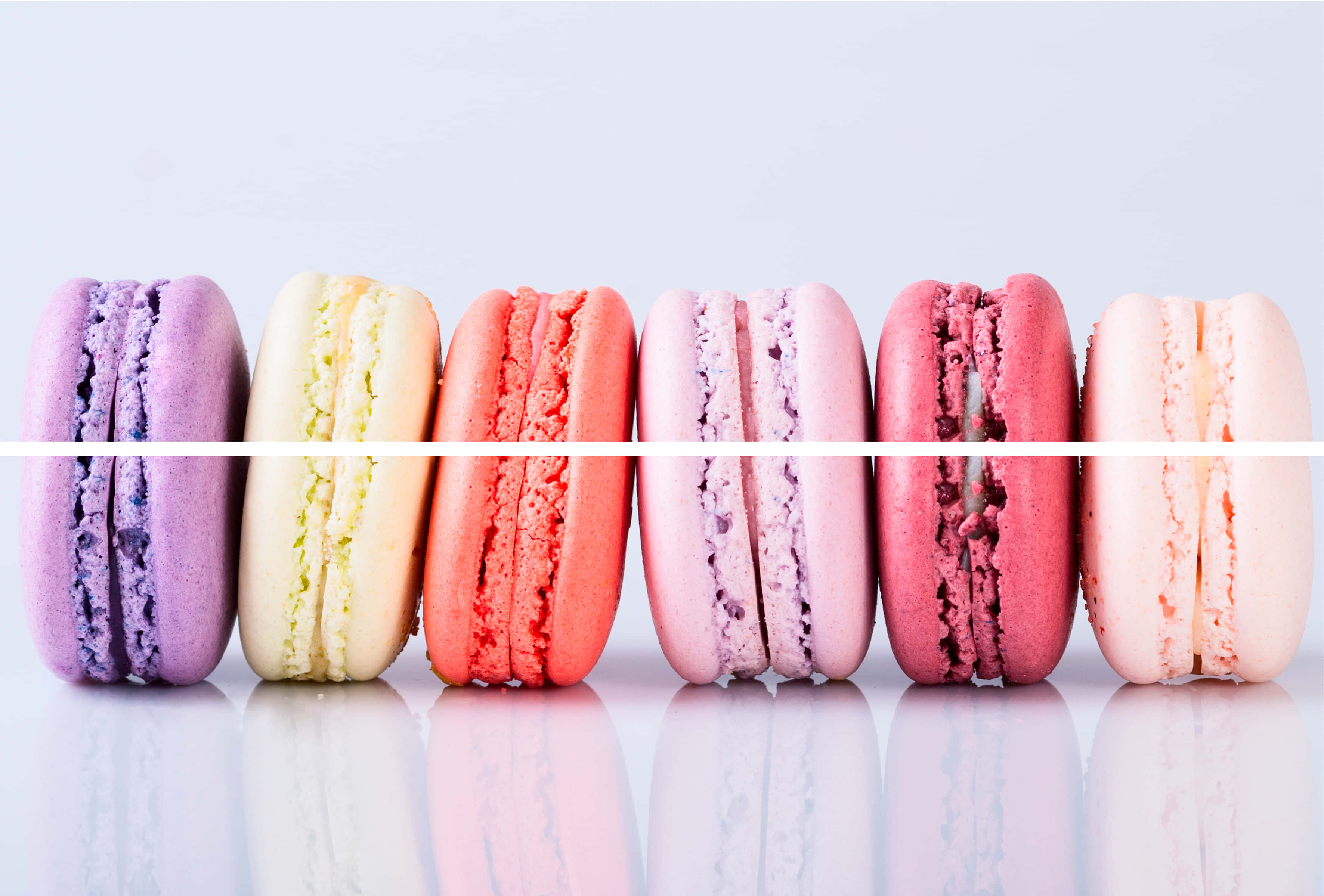 Macaron 桌布 壁紙 — 六款色彩繽紛的馬卡龍以柔和色調排列在反光表面上，襯托柔軟的白色背景。