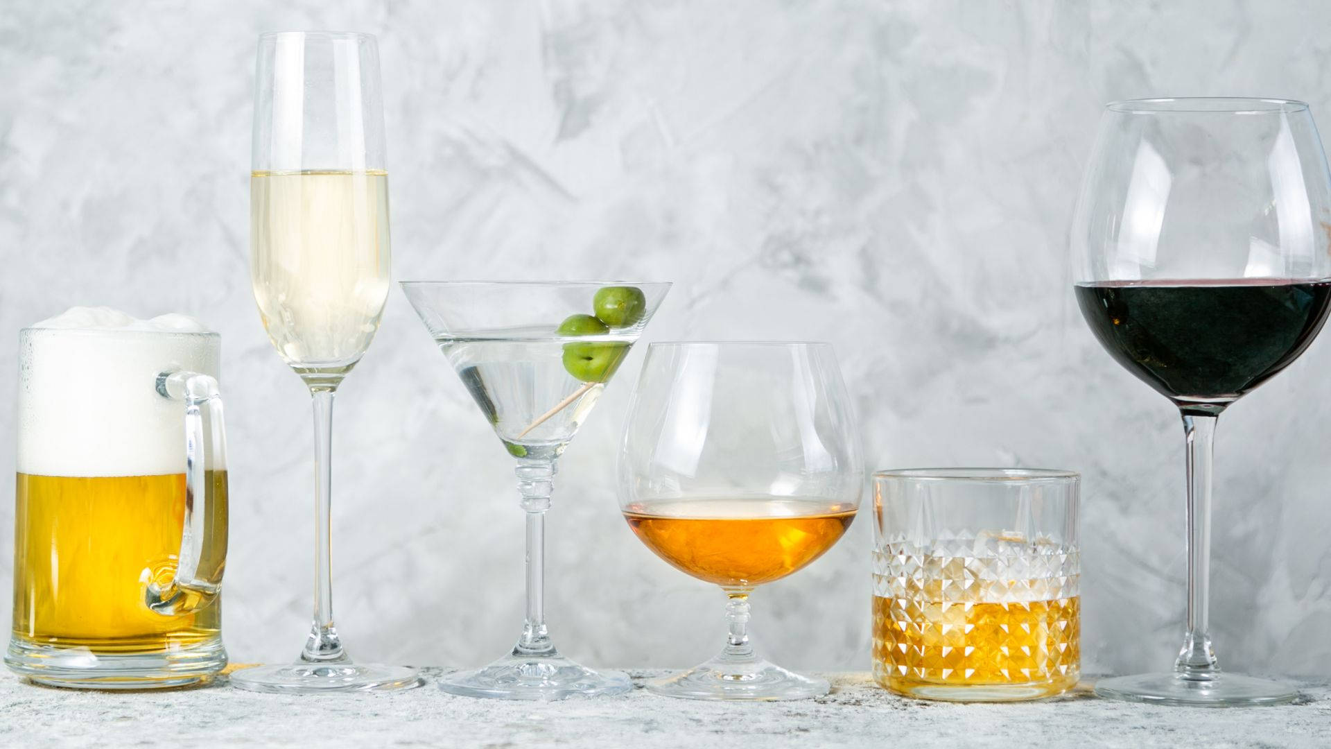 alcohol 桌布 壁紙 — 六種不同的酒精飲料，包括啤酒、香檳、馬丁尼、威士忌和葡萄酒，優雅地排列在有紋理的灰色表面上。