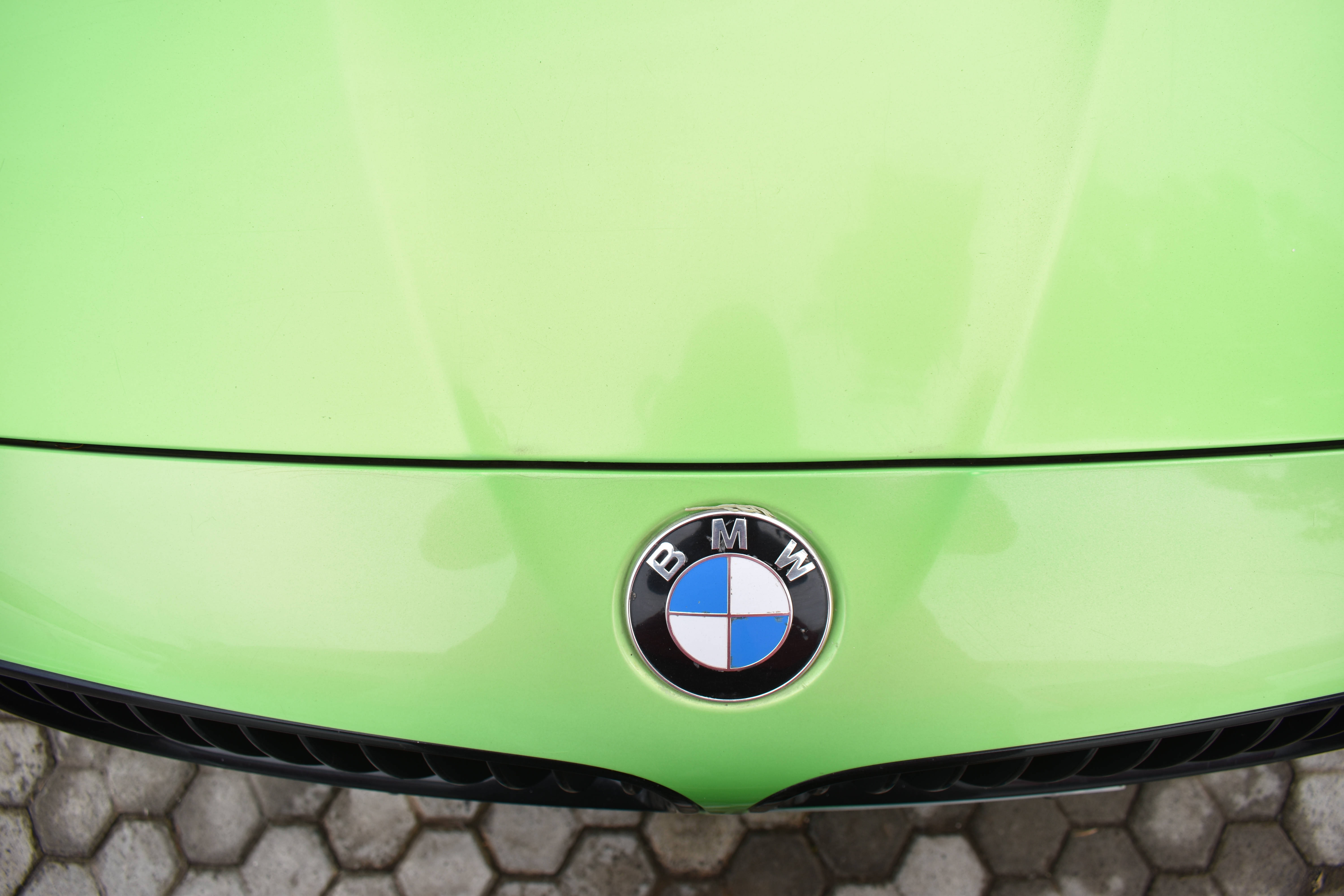 m 桌布 壁紙 — 六角形路面上一塊充滿活力的萊姆綠色BMW引擎蓋特寫，標誌性圓形標誌居中位於黑色格柵上方。
