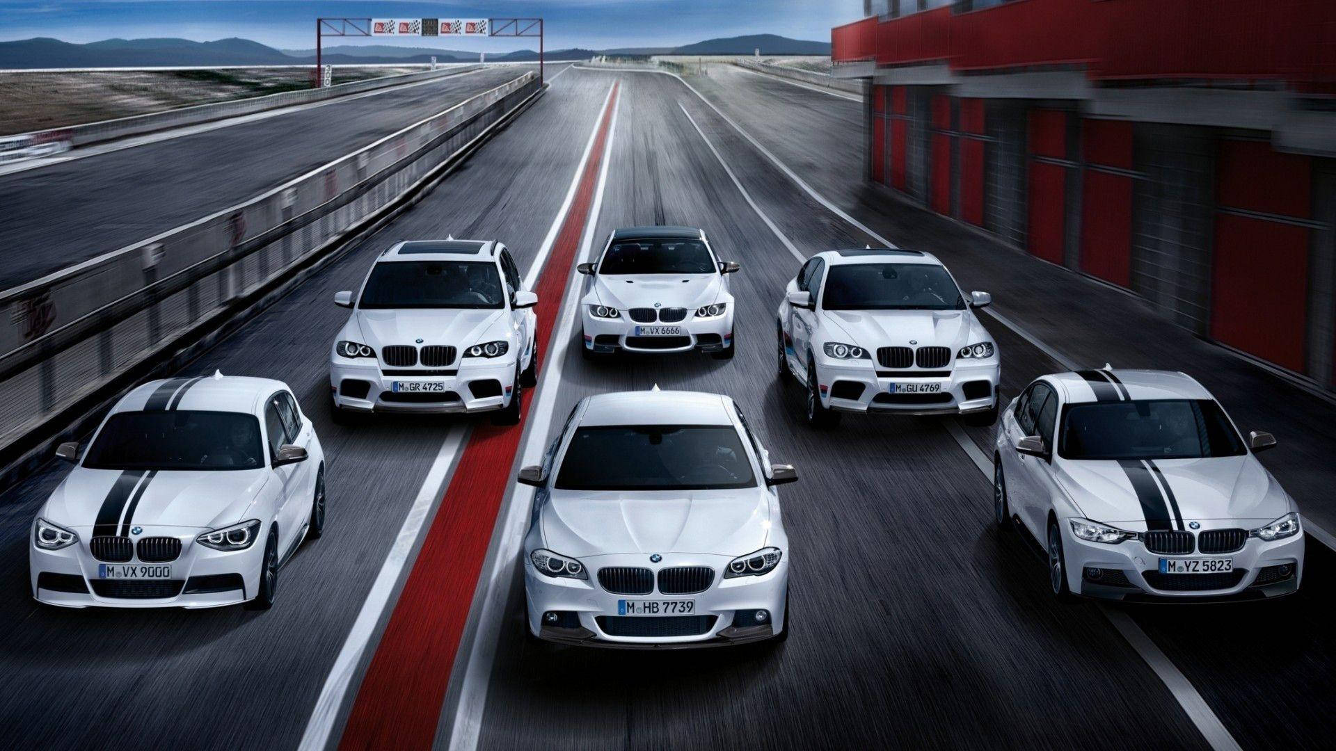 m 桌布 壁紙 — 六輛白色BMW高性能賽車在陰天下行駛在一條有紅白條紋的蜿蜒賽道上。
