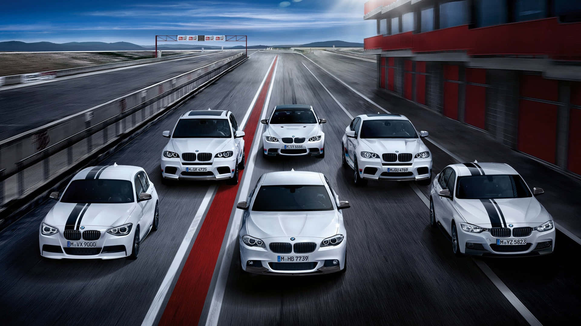 BMW 動圖 桌布 壁紙 — 六輛白色BMW高性能賽車在陰天下的紅白條紋賽道上奔馳。