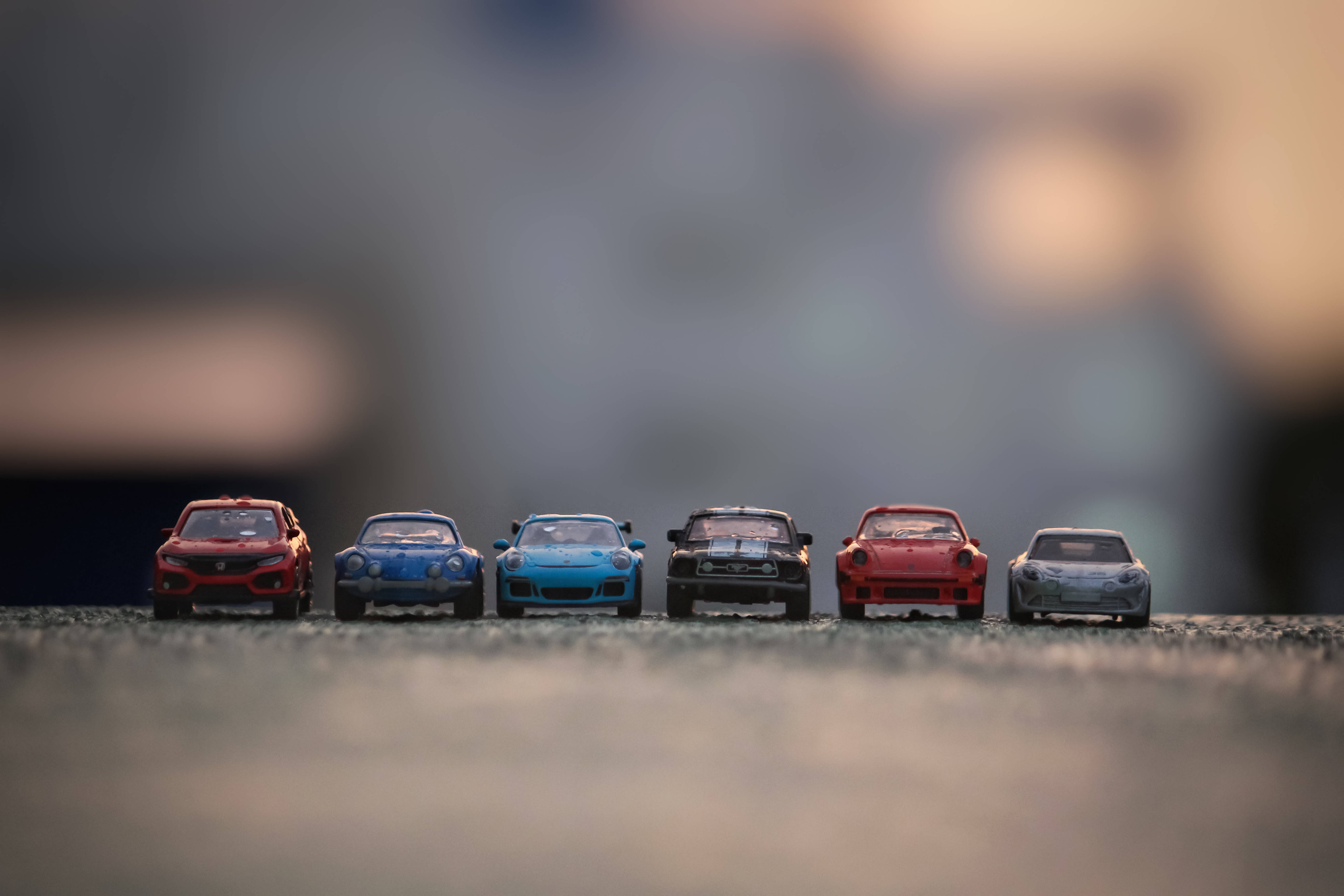 mustang HD 桌布 壁紙 — 六輛色彩繽紛的玩具跑車排列在帶有紋理的表面上，背景柔和模糊，沐浴在溫暖的金色光芒中。